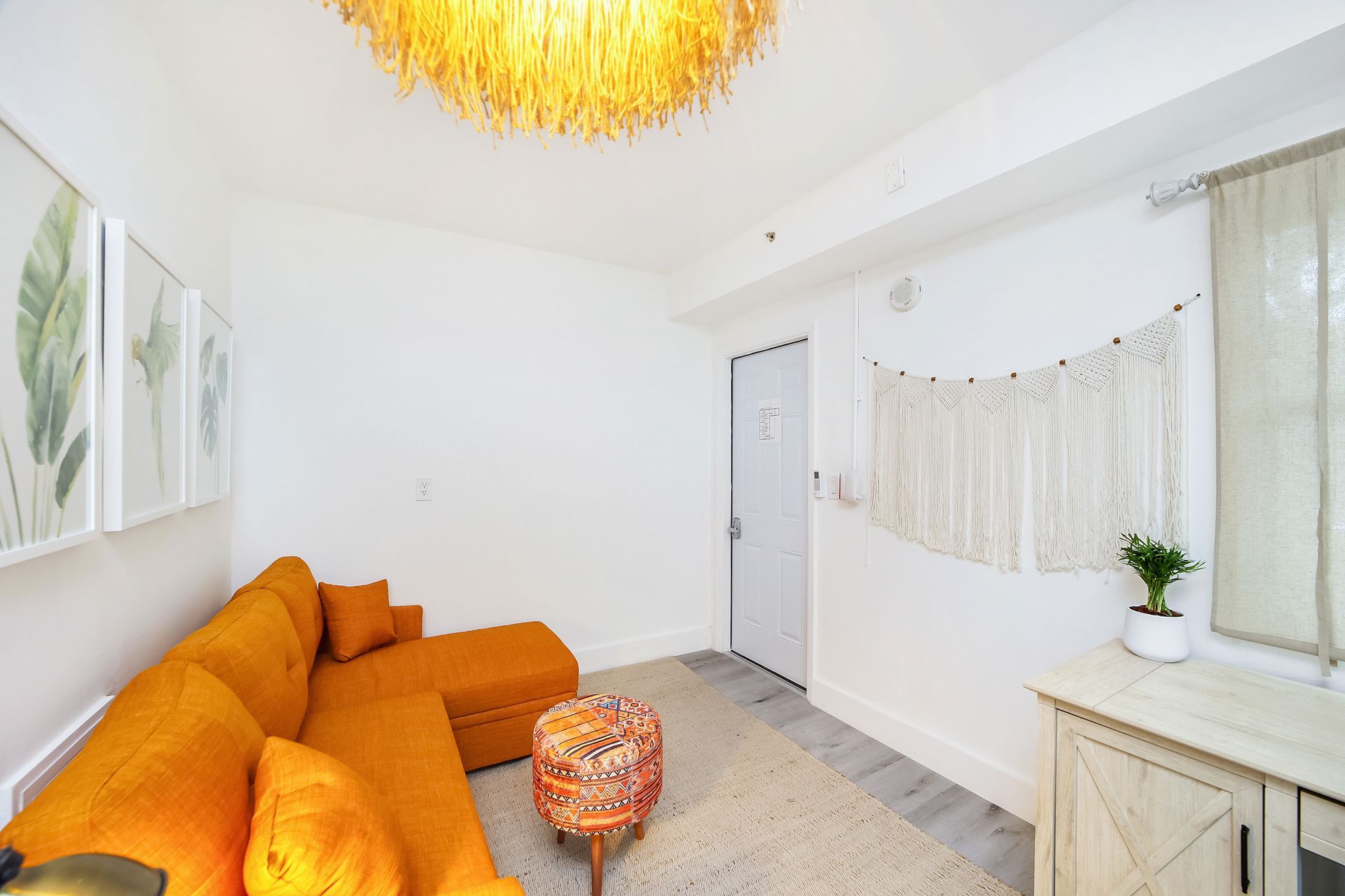 Cozy room with an orange sectional, macrame wall hanging, and wooden cabinet.