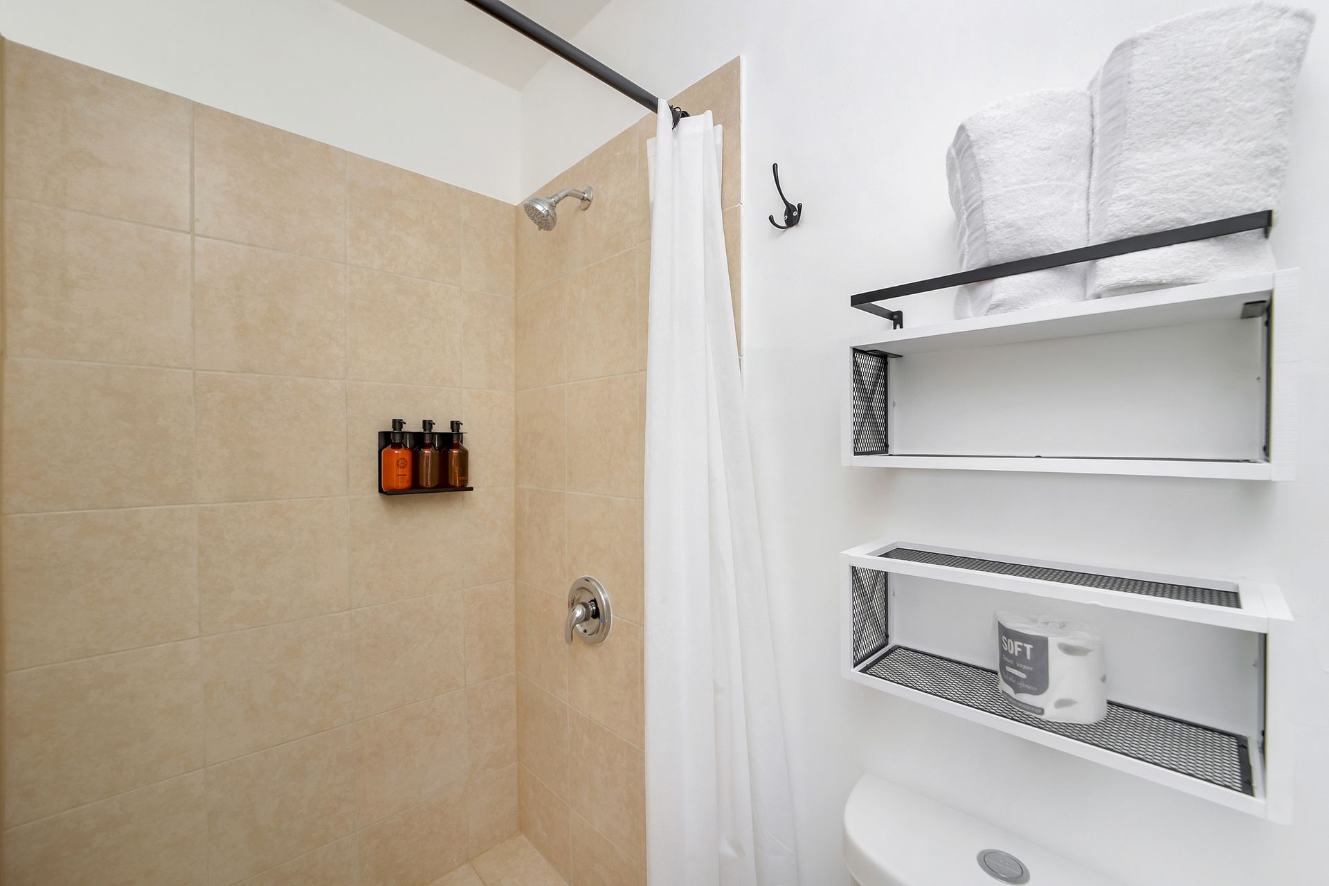 Small bathroom with a tan tiled shower, white shelves, and a toilet.