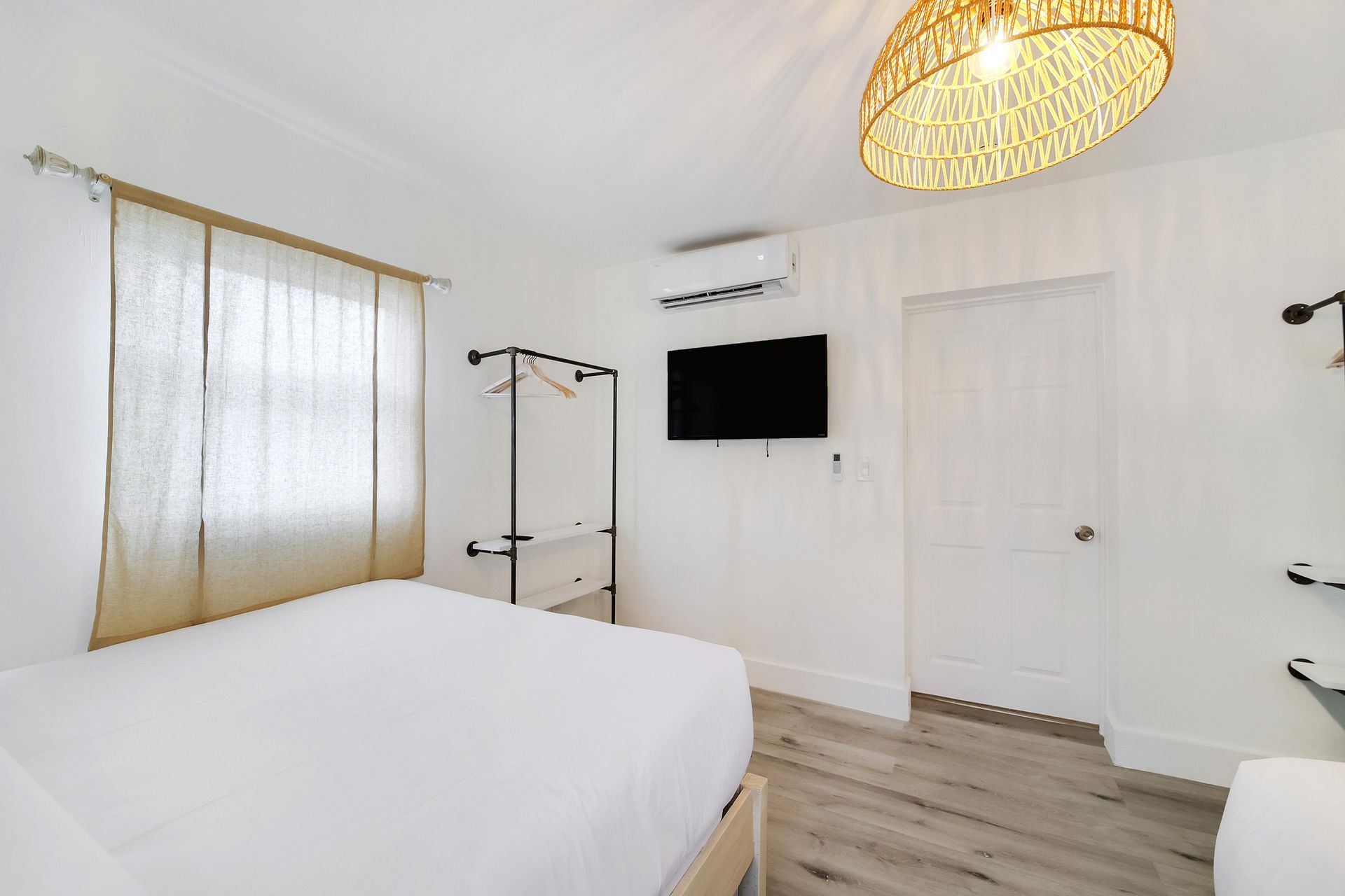Bedroom with white walls, bed, window with curtains, TV, clothes rack, light fixture.