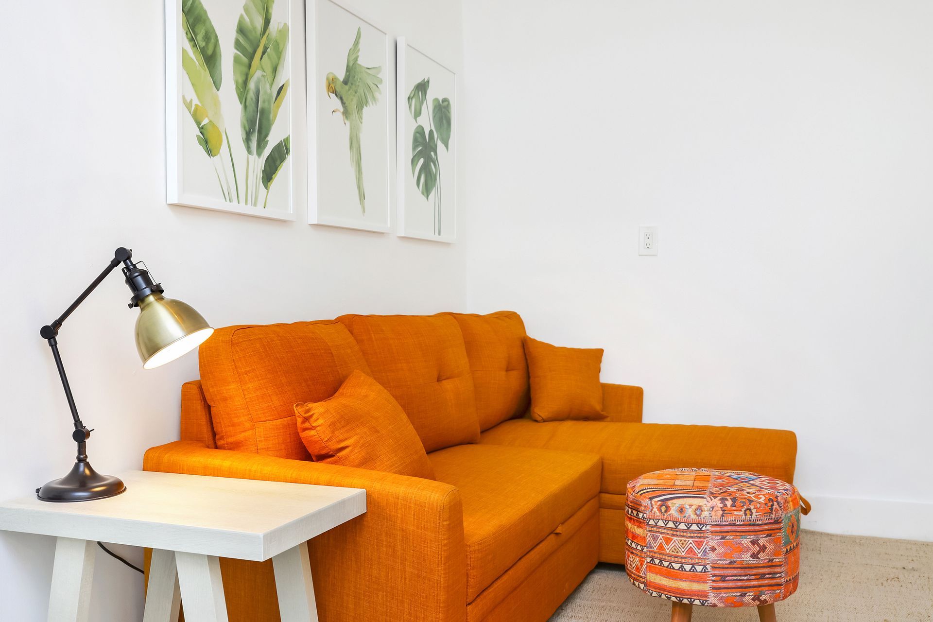 Orange sectional sofa with side table, lamp, and art on white wall.