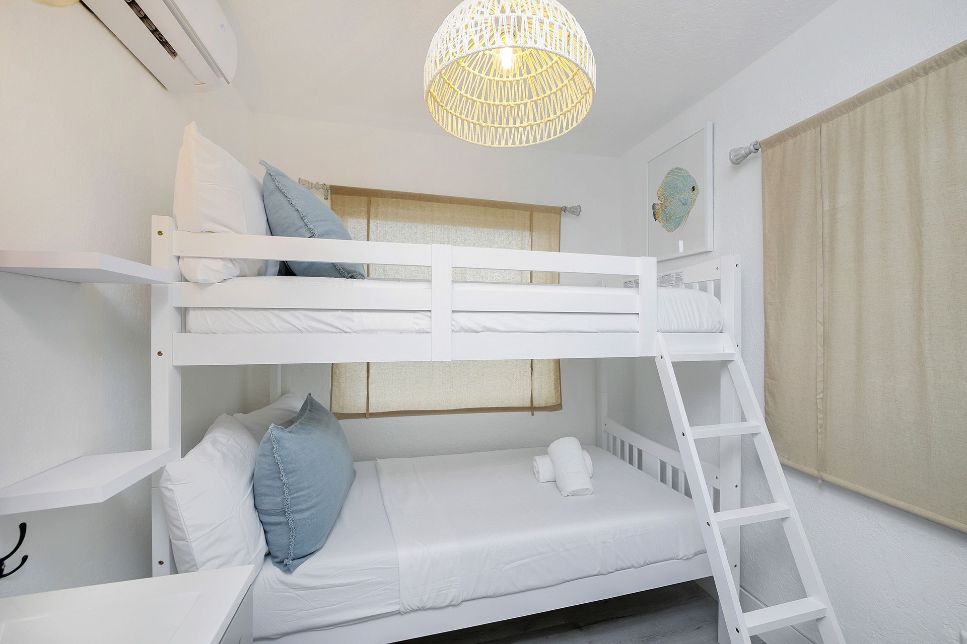 White bunk beds in a bright room with light blue pillows and a woven light fixture.