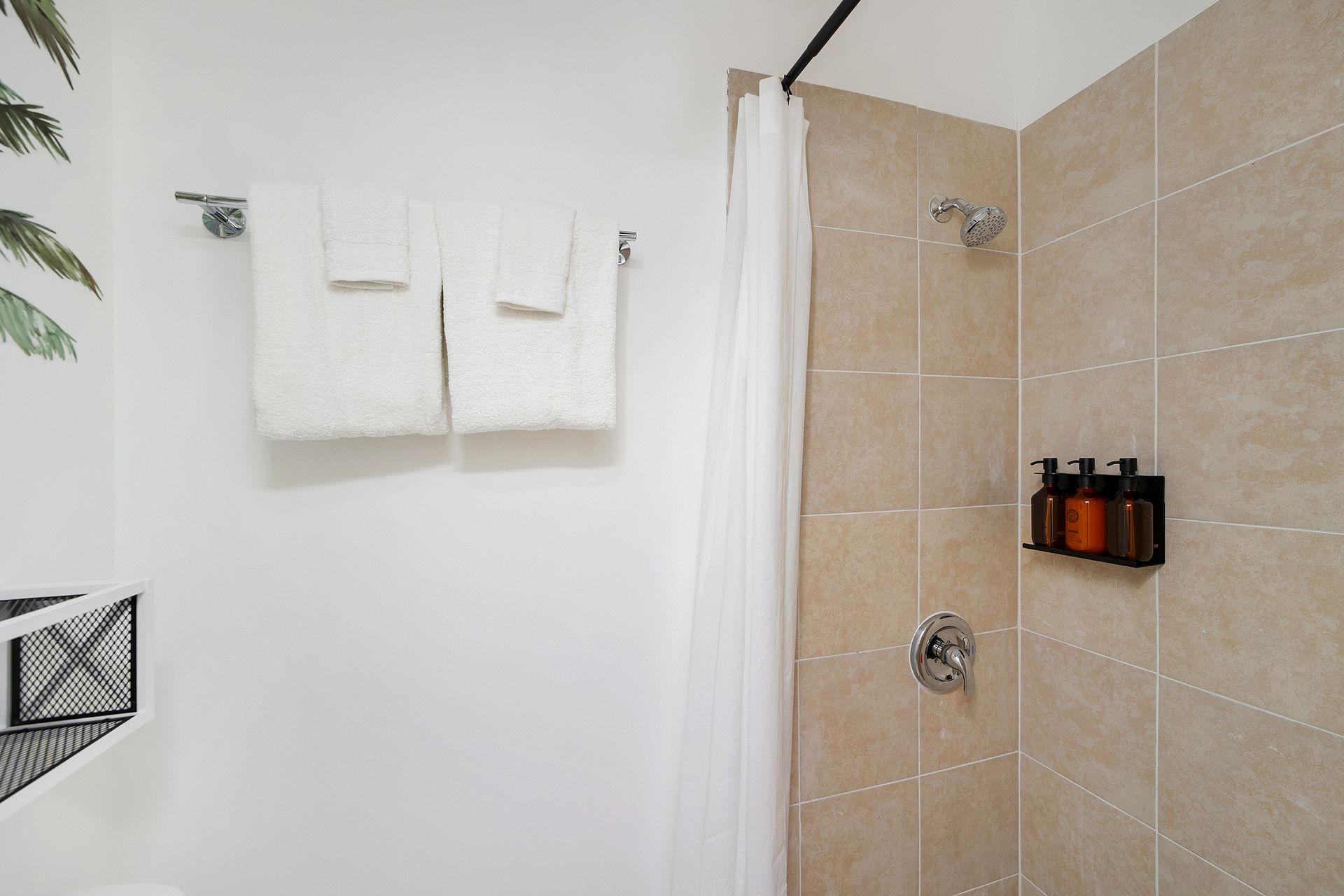 Bathroom with shower, tan tiles, white shower curtain, towels on rack.