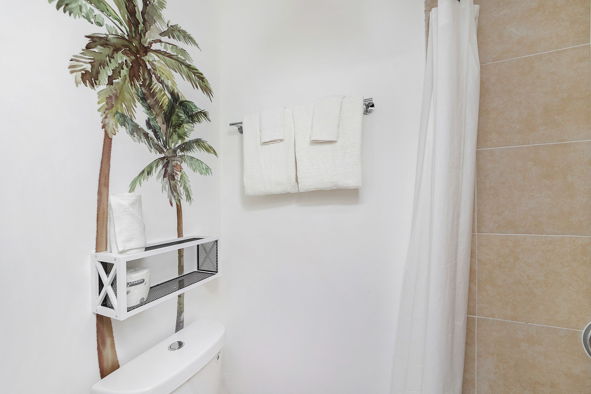 Bathroom with palm tree mural, white towels on rack, and a shower with white curtain.
