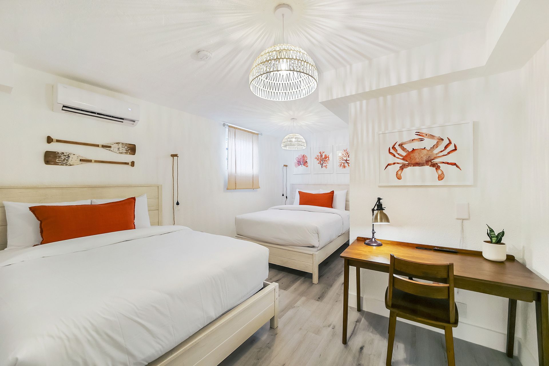 Bright white bedroom with two beds, an orange crab artwork, and a desk.