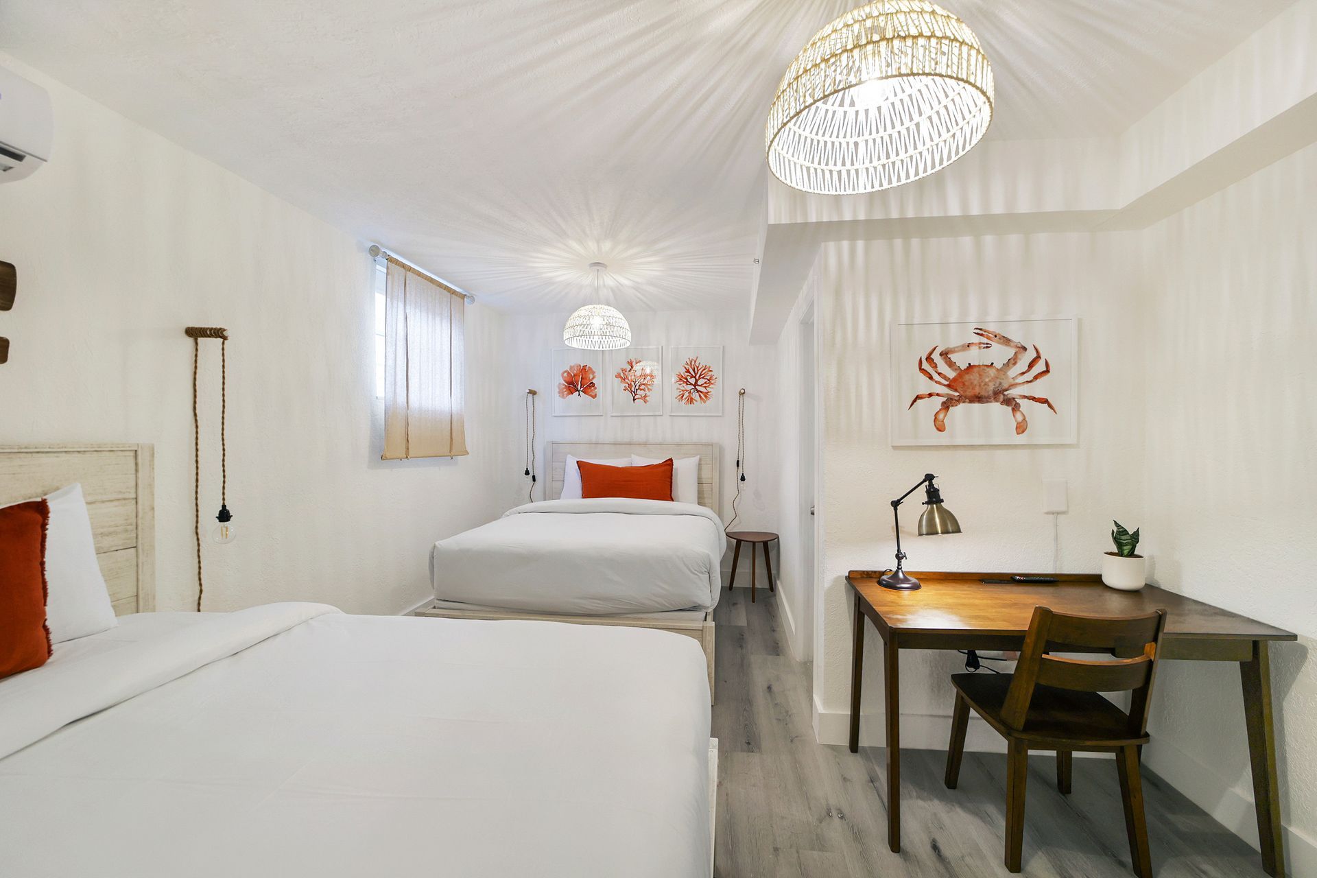 White bedroom with two beds, a desk, and beach-themed art.