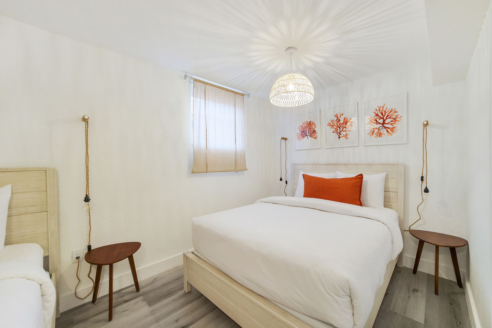 A bright, white bedroom with two beds, coral artwork, and wooden accents.