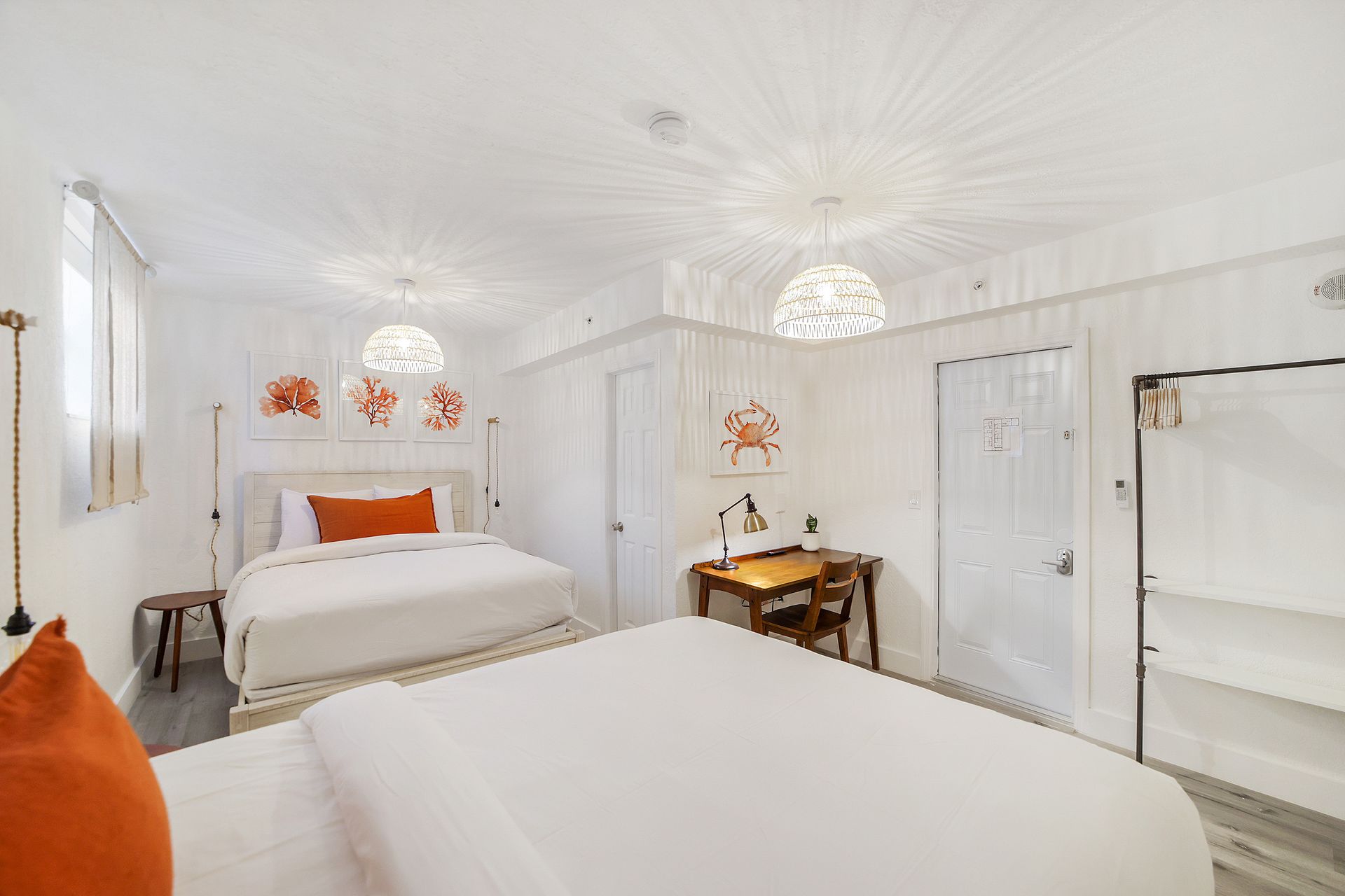 Bright, white hotel room with two beds, small desk, artwork, and open closet.