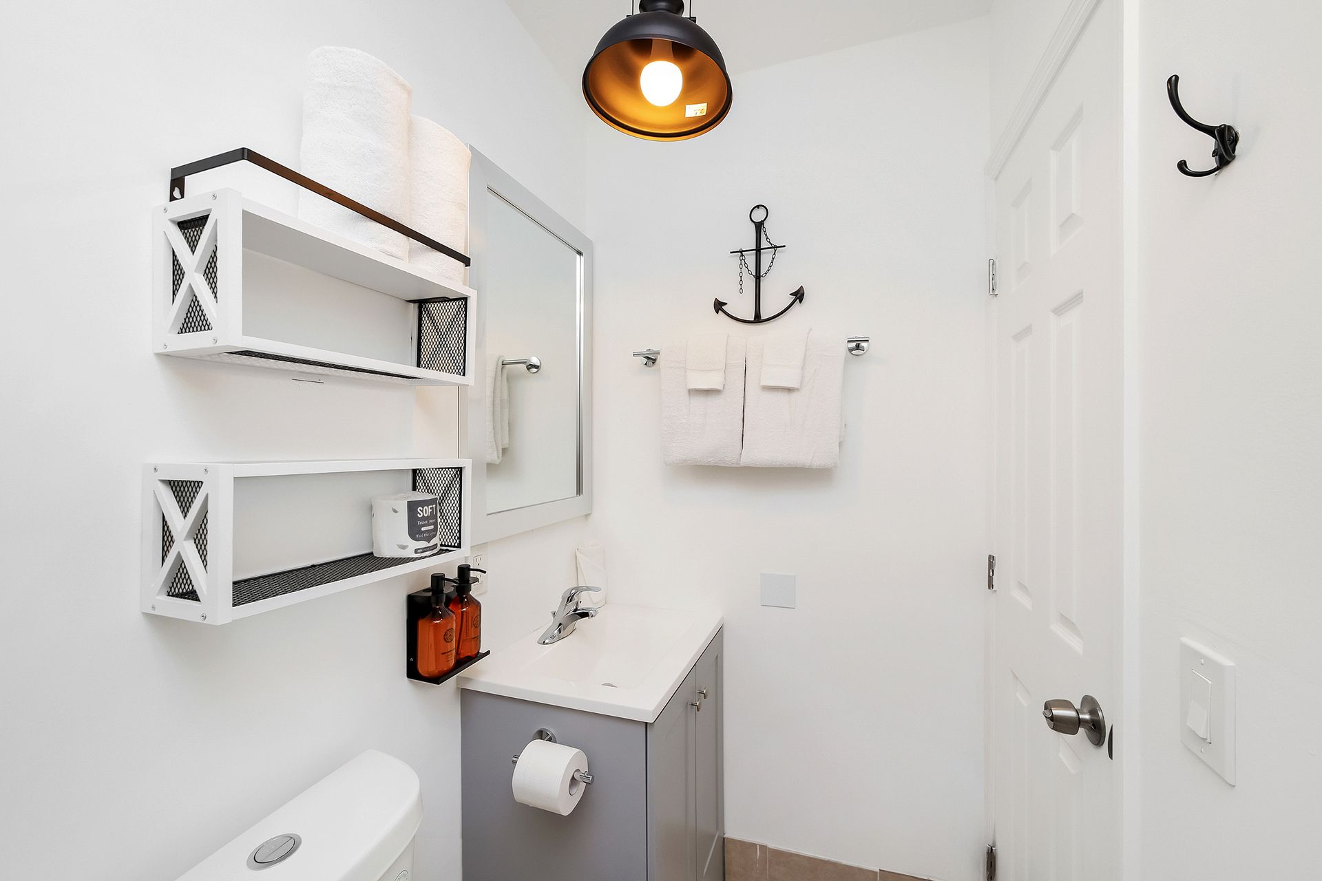 Small bathroom with white walls, gray vanity, and decorative shelves.
