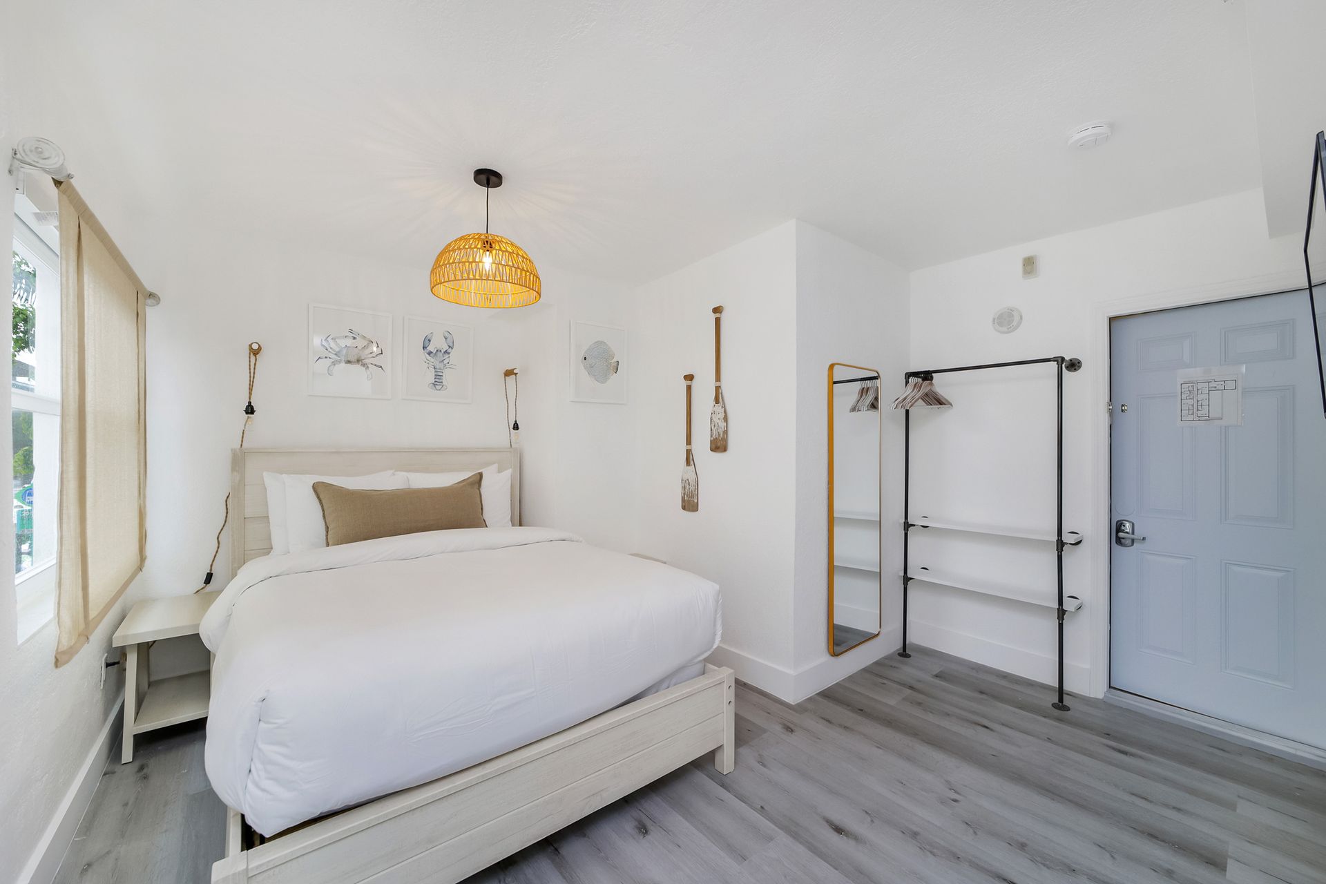 Bedroom with white walls, bed, open wardrobe, light wood floor, and blue door.
