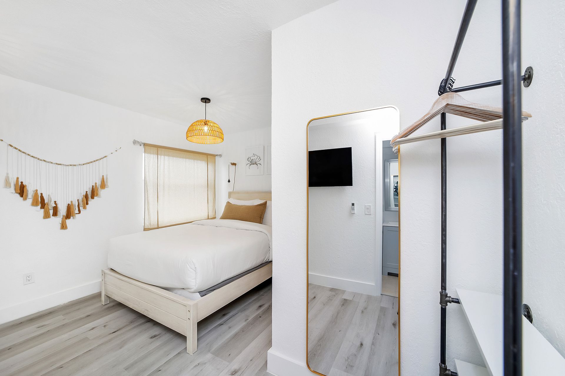 White bedroom with a single bed, full-length mirror, wall-mounted TV, and hanging clothes rack.