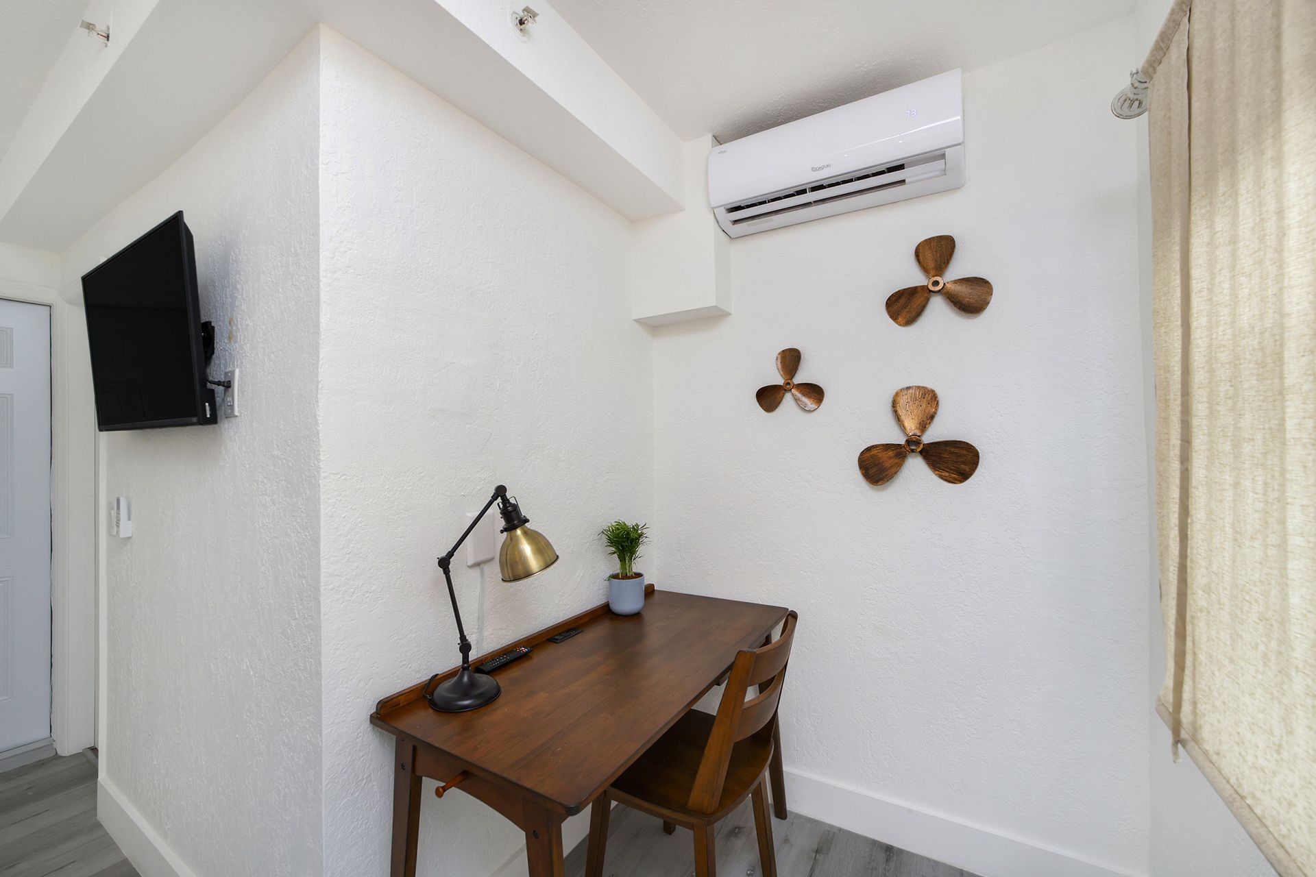A small office nook with a desk, chair, mounted TV, and decorative bronze fan blades.