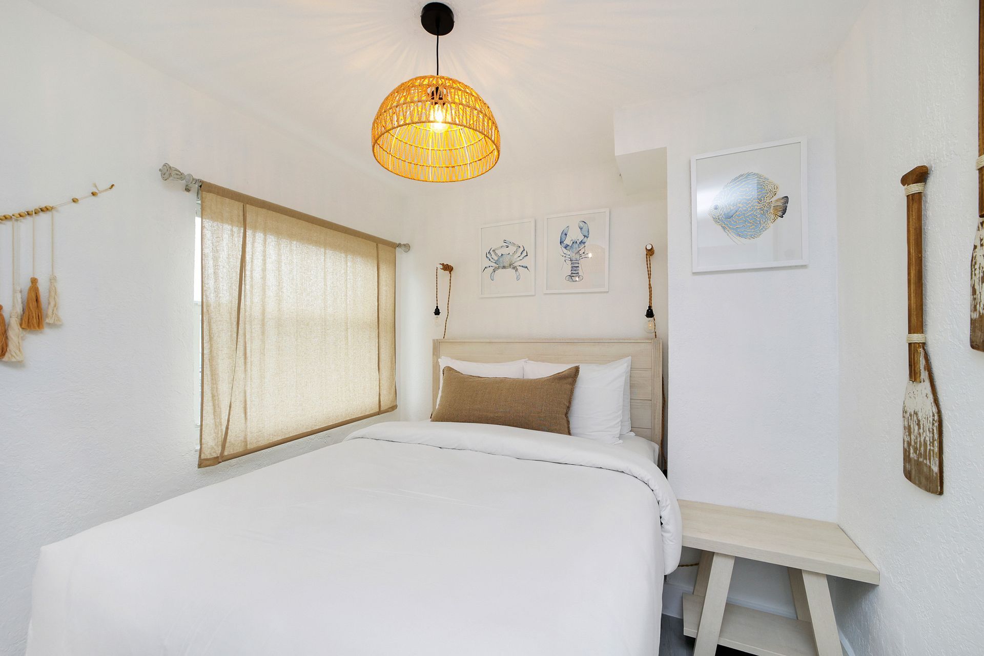 Bedroom with white walls, bed, woven light fixture, and nautical decor.