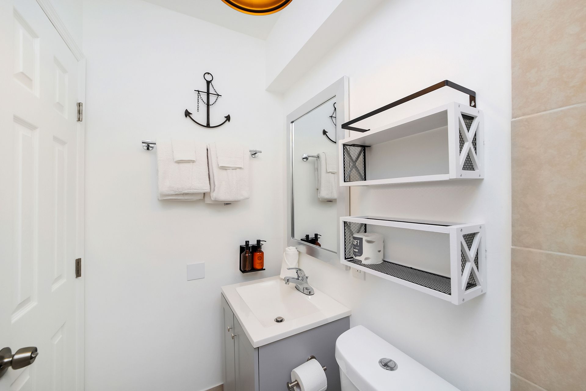 Small white bathroom with sink, toilet, shelves, towels, and anchor decor.