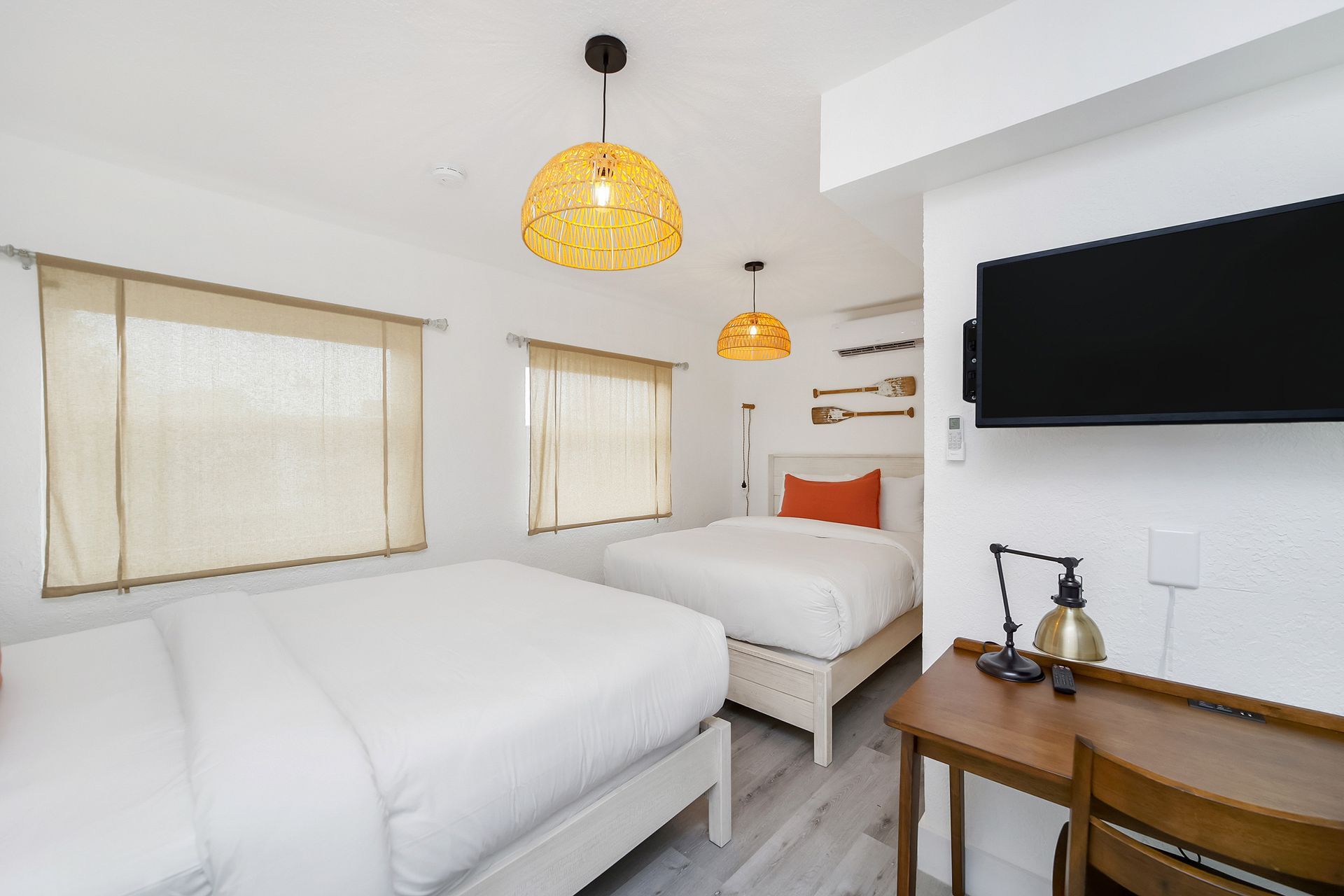 Bedroom with two white beds, desk, TV, and woven pendant lights.