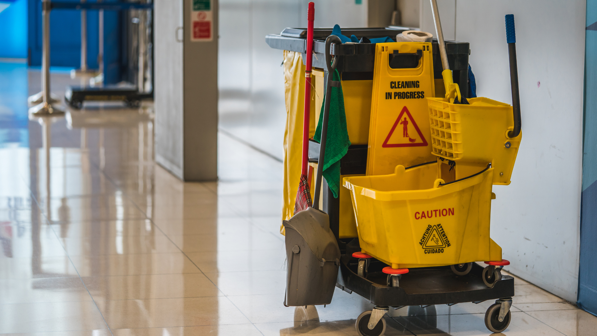 A yellow mop bucket is on a cart in a hallway.