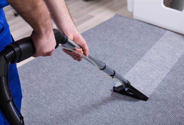 A man is cleaning a carpet with a vacuum cleaner.