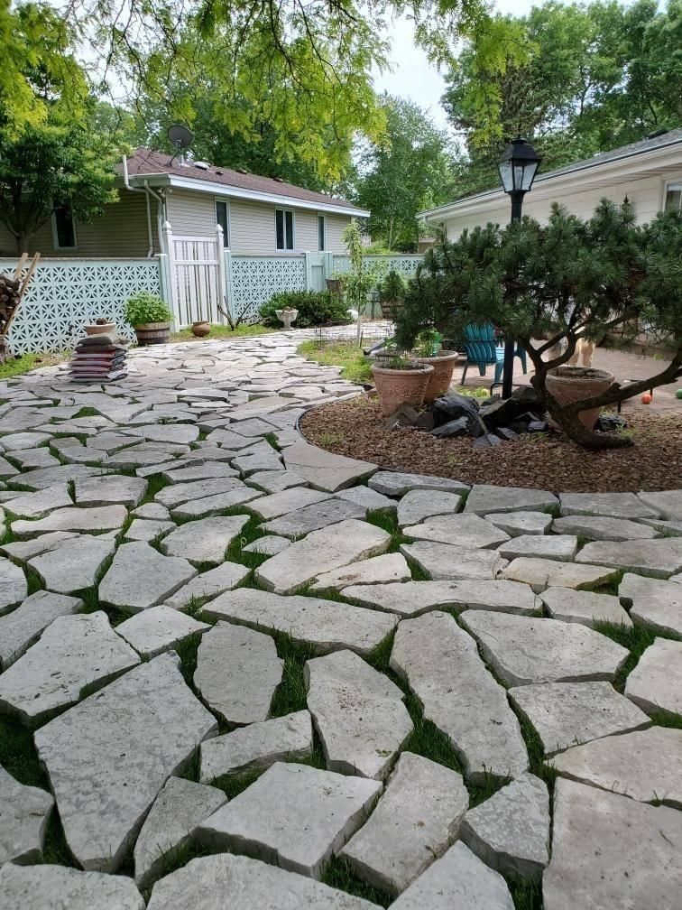 A backyard stone path made of irregular flagstones set with grass, leading past a landscaped area with a small tree.