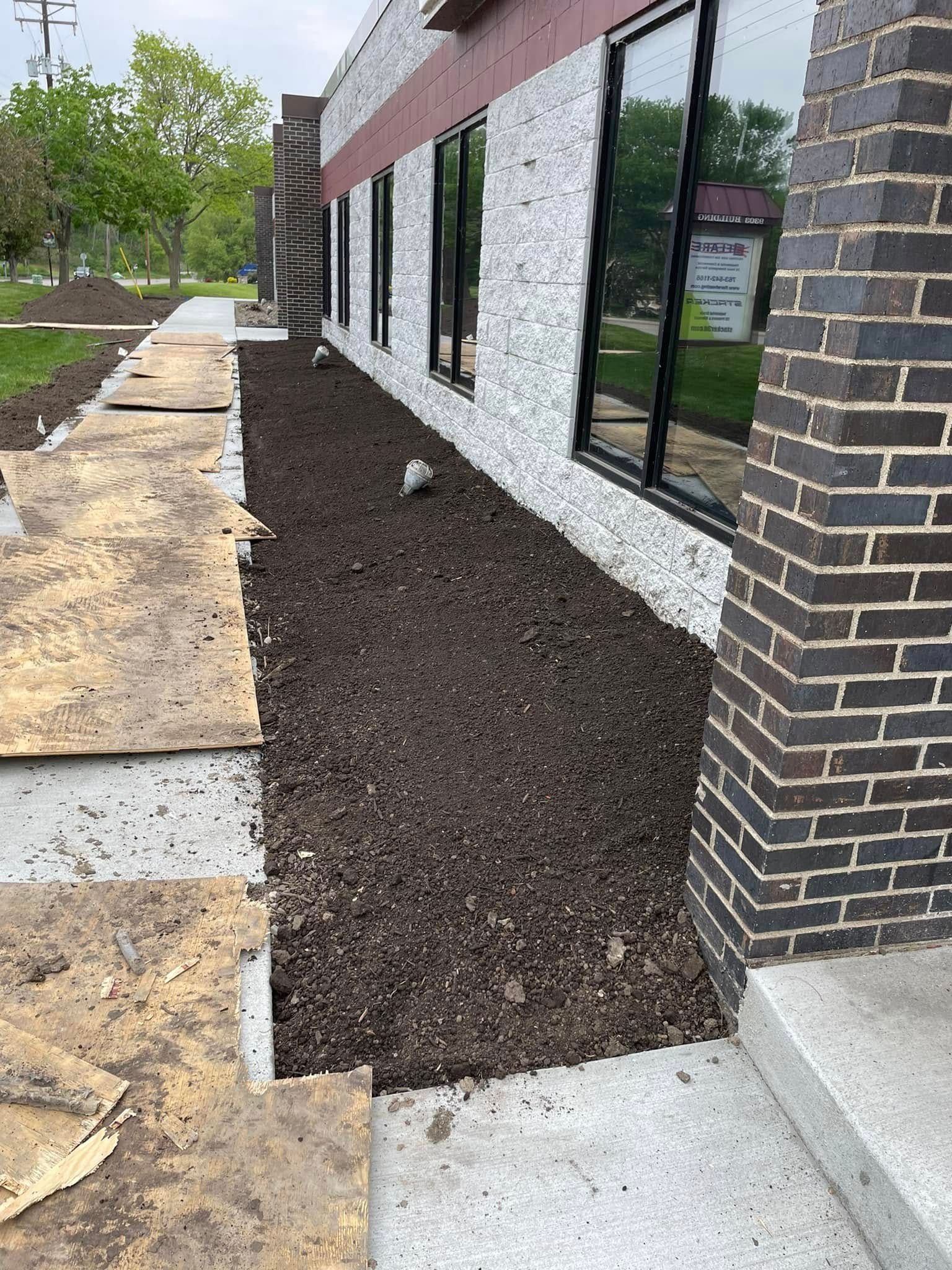 A side view of a building exterior with a newly mulched landscape bed, dark brick corner, and a concrete walkway.