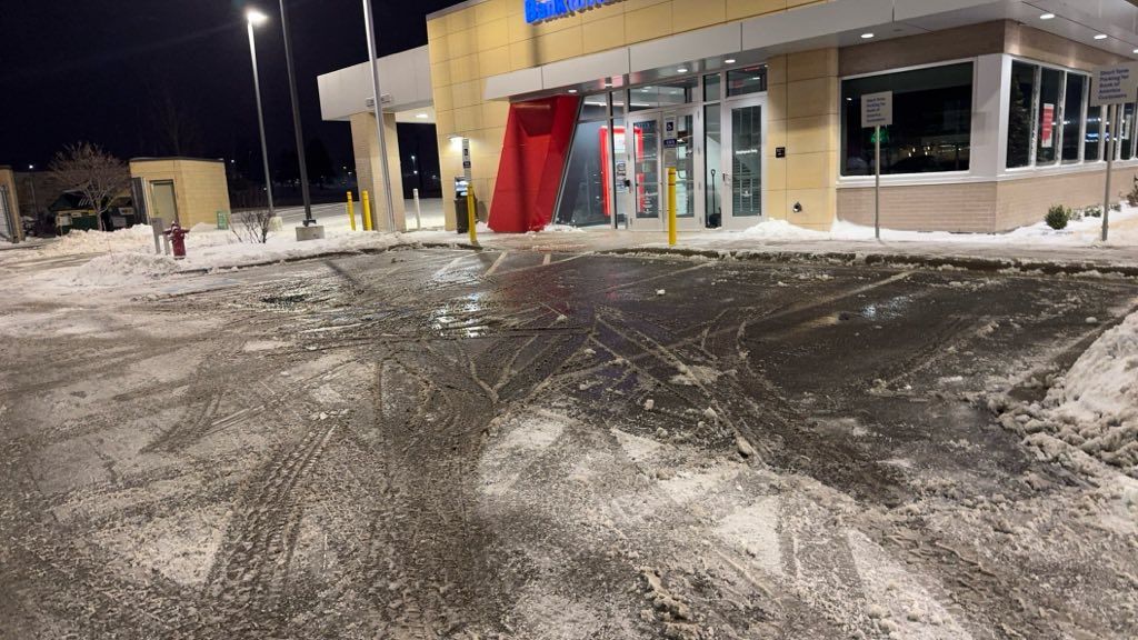 A slushy, snow-covered parking lot at night in front of a brightly lit building with a red banner over the entrance.