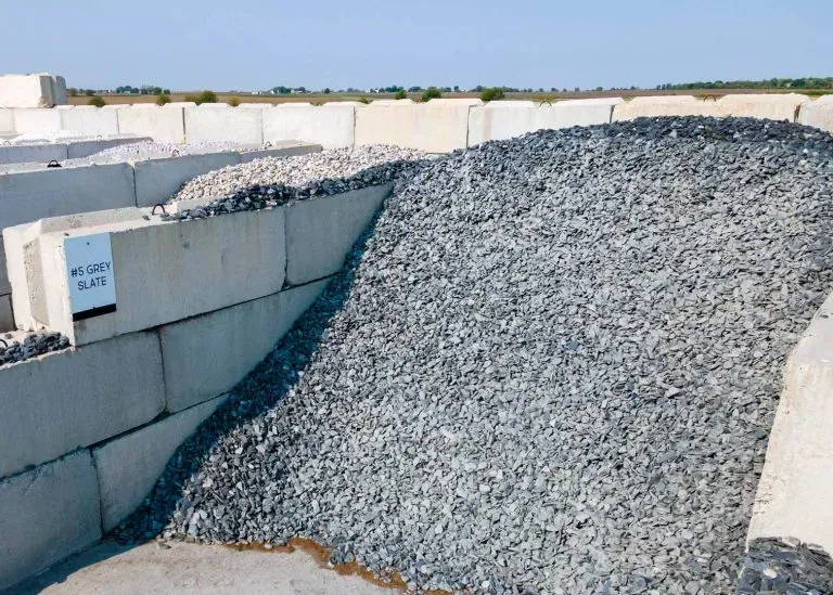 A large pile of dark gray gravel contained within a structured bay made of stacked concrete blocks.