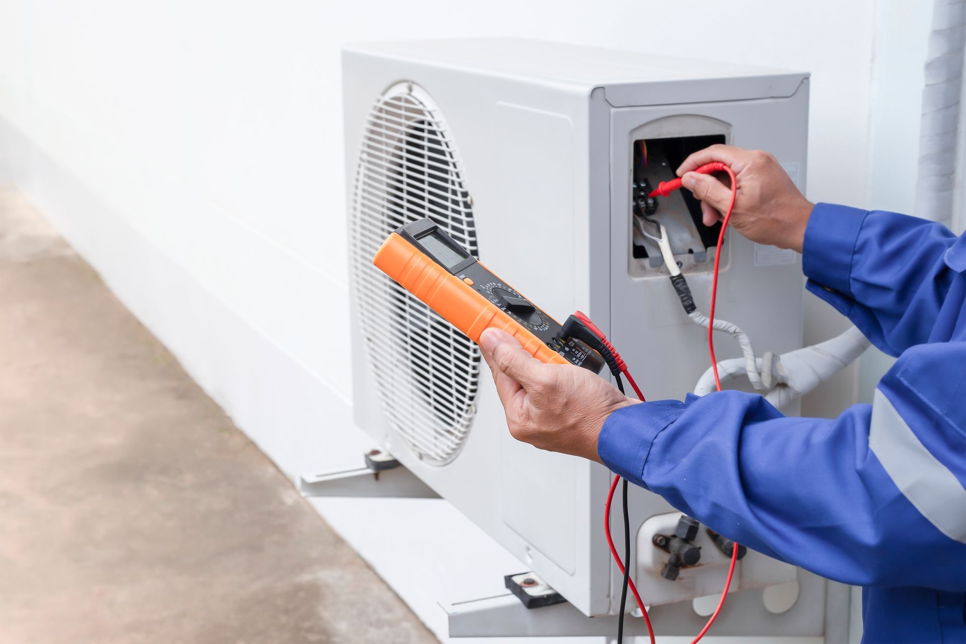 A man is fixing an air conditioner with a multimeter.