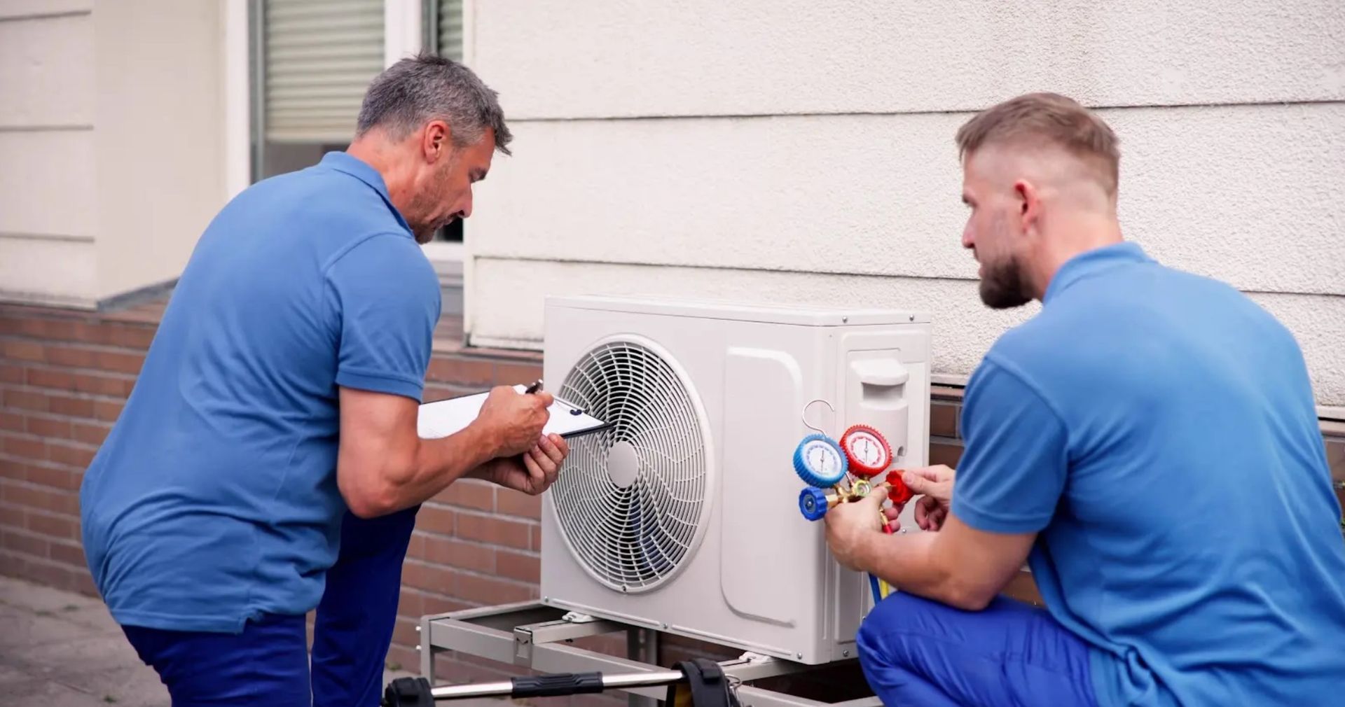 Two men are working on an air conditioner outside of a building.