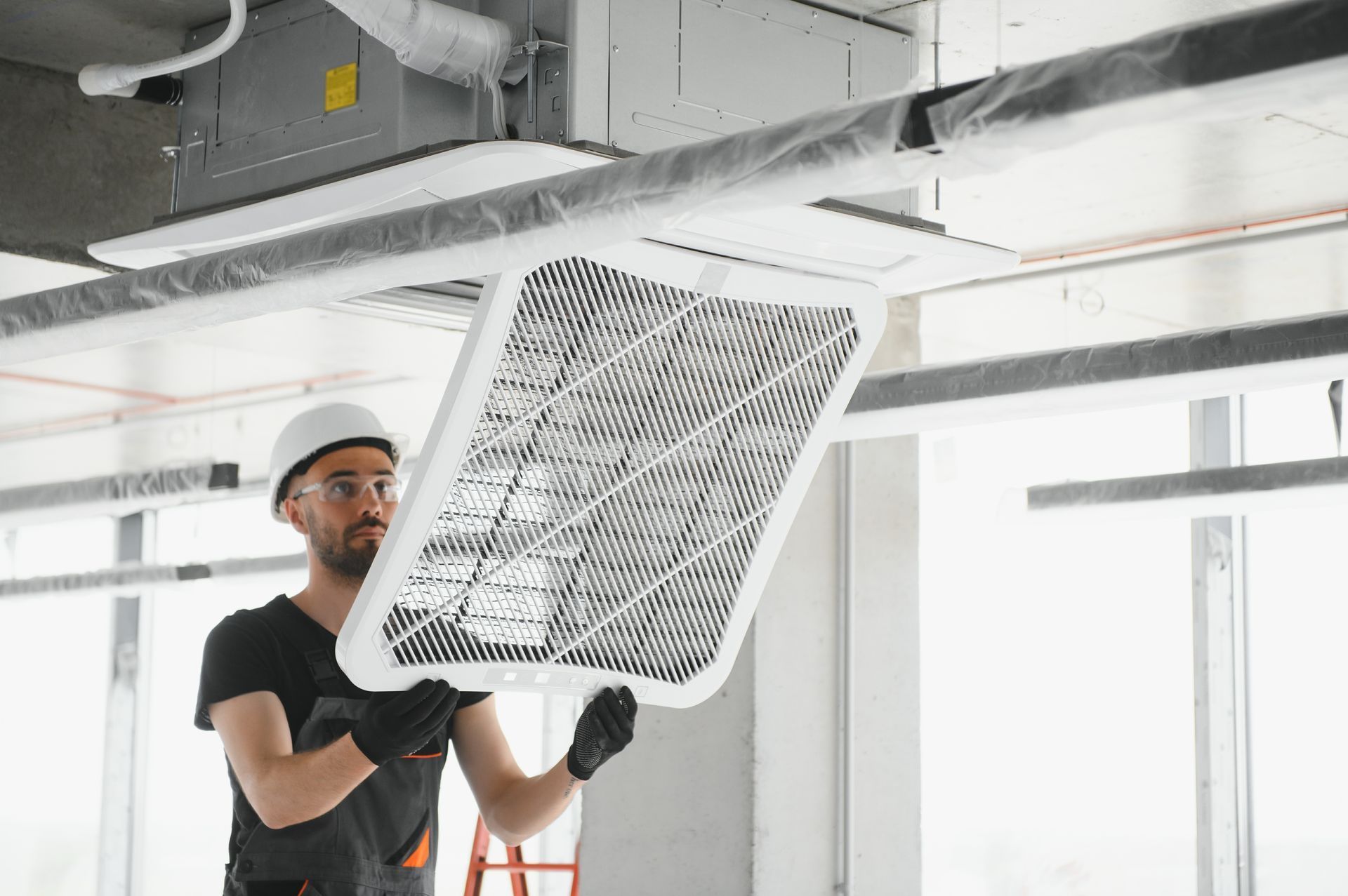 Construction worker installing a ceiling air vent. He wears a hard hat, and gloves.