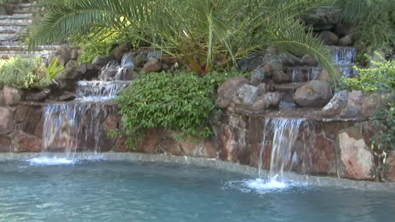 A waterfall is surrounded by rocks and trees next to a swimming pool.