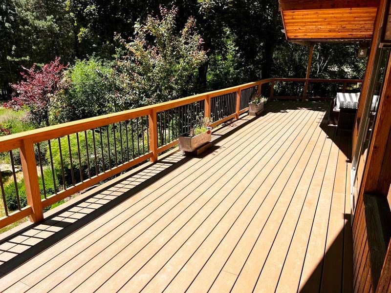 A large wooden deck with a wooden railing and trees in the background.