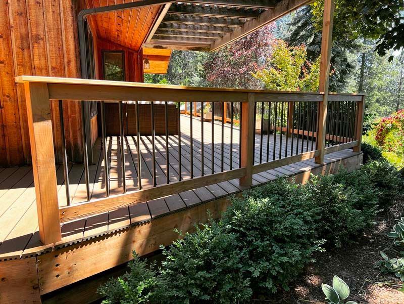 A wooden deck with a metal railing and a wooden house in the background.