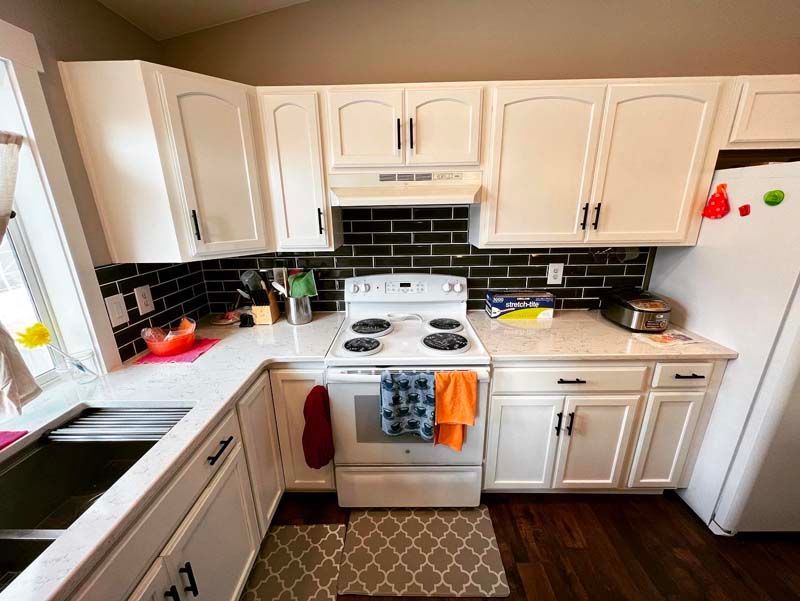 A kitchen with white cabinets , a stove , a sink , and a refrigerator.
