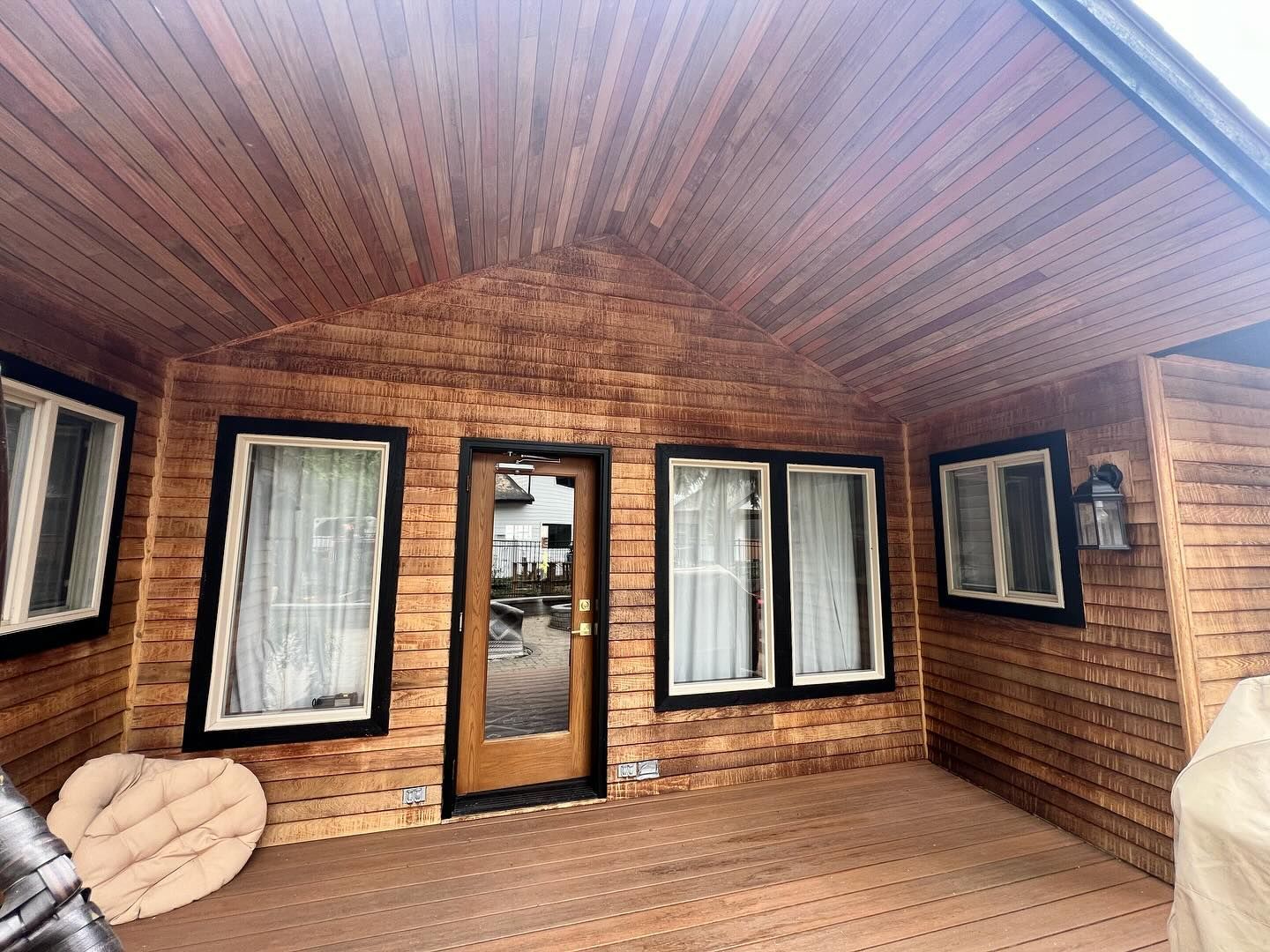 A wooden porch with a door and windows on a house.