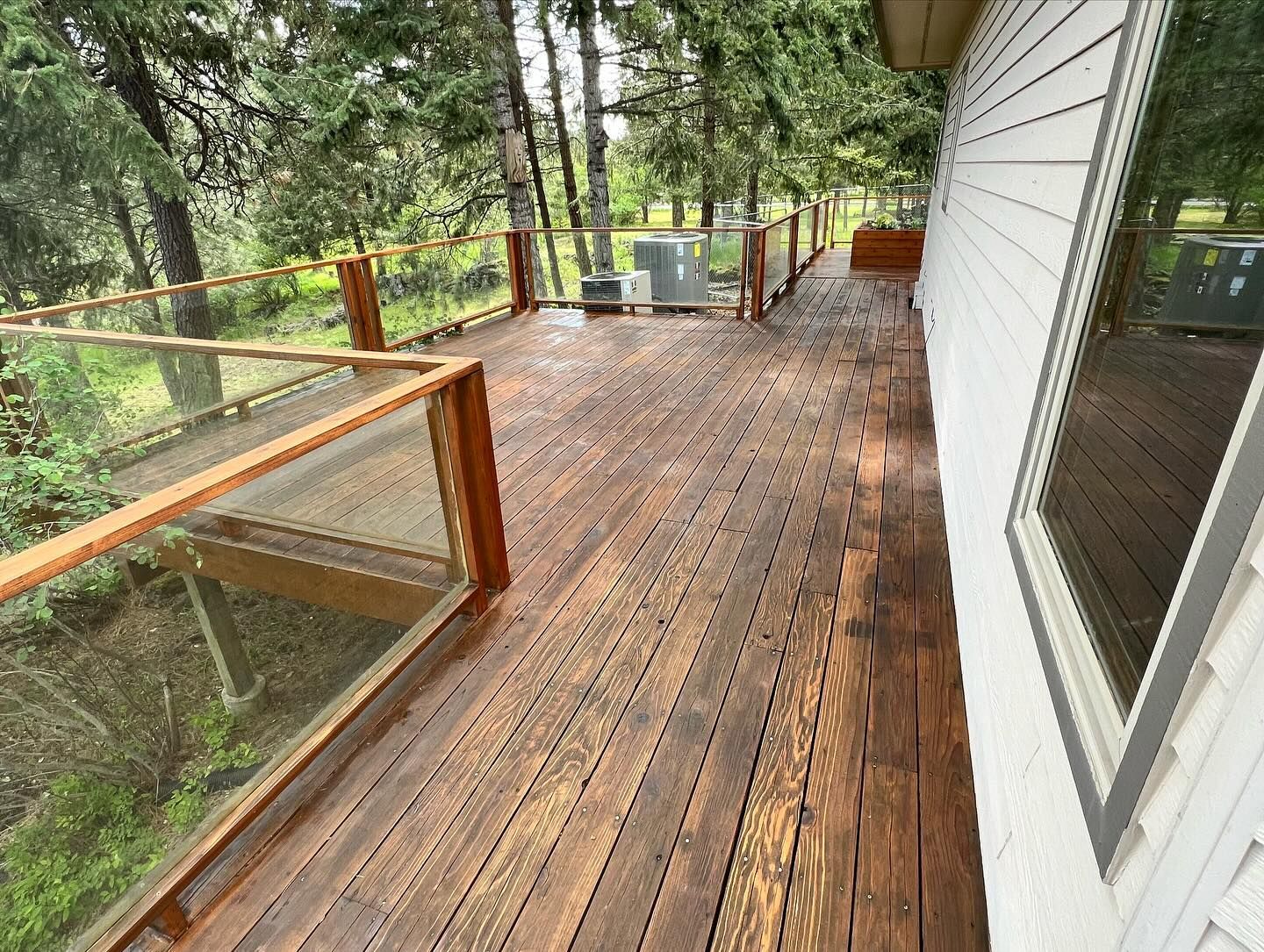 A wooden deck with a glass railing and trees in the background.