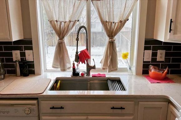 A kitchen with a sink and a window with curtains.