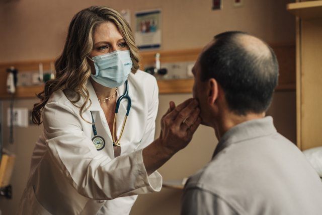 A doctor wearing a mask is examining a patient 's face in a hospital room.