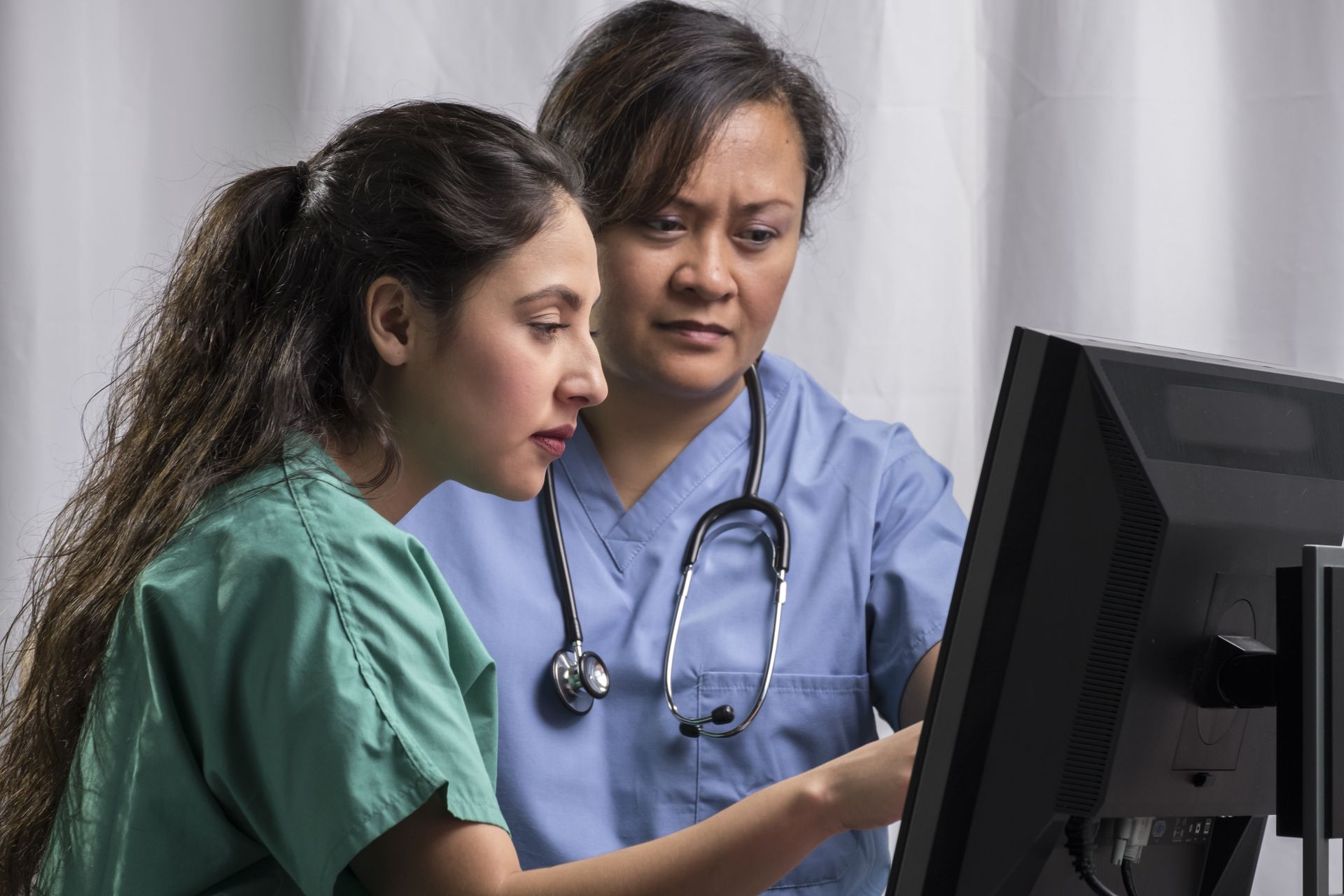 Two nurses are looking at a computer screen together.