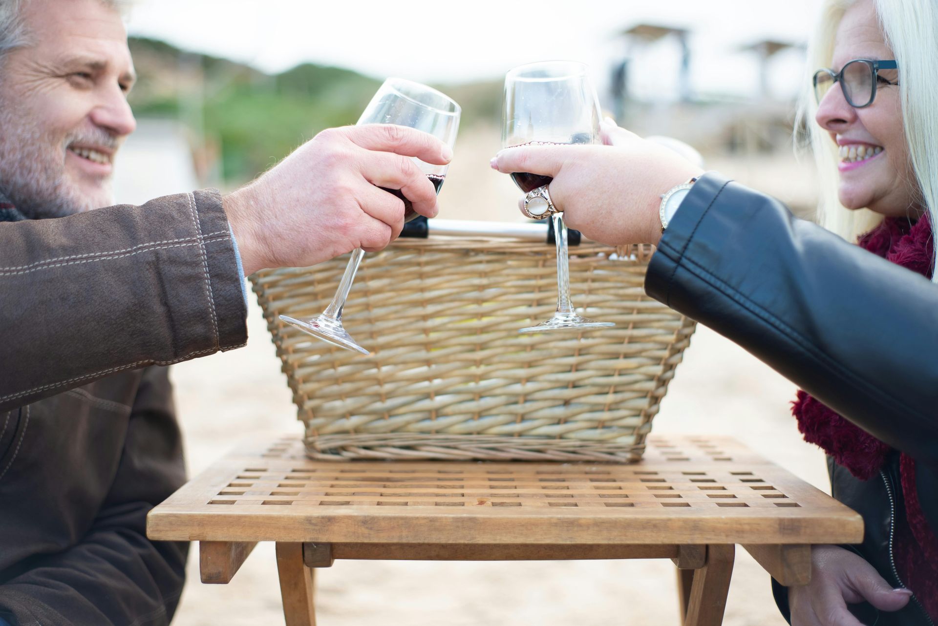 Older couple toasting with wine glasses at a picnic on the beach.
