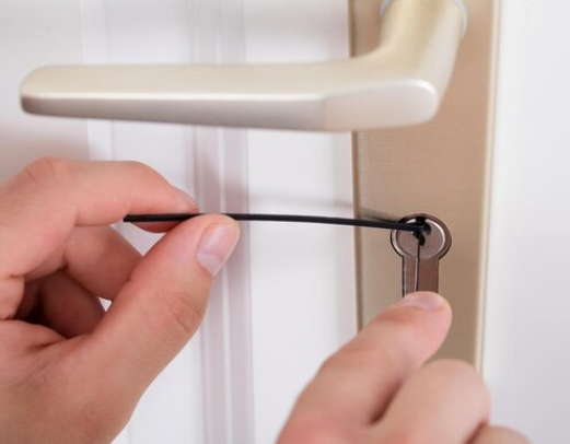 Manos que utilizan un cordón negro para manipular una llave en la cerradura de una puerta.