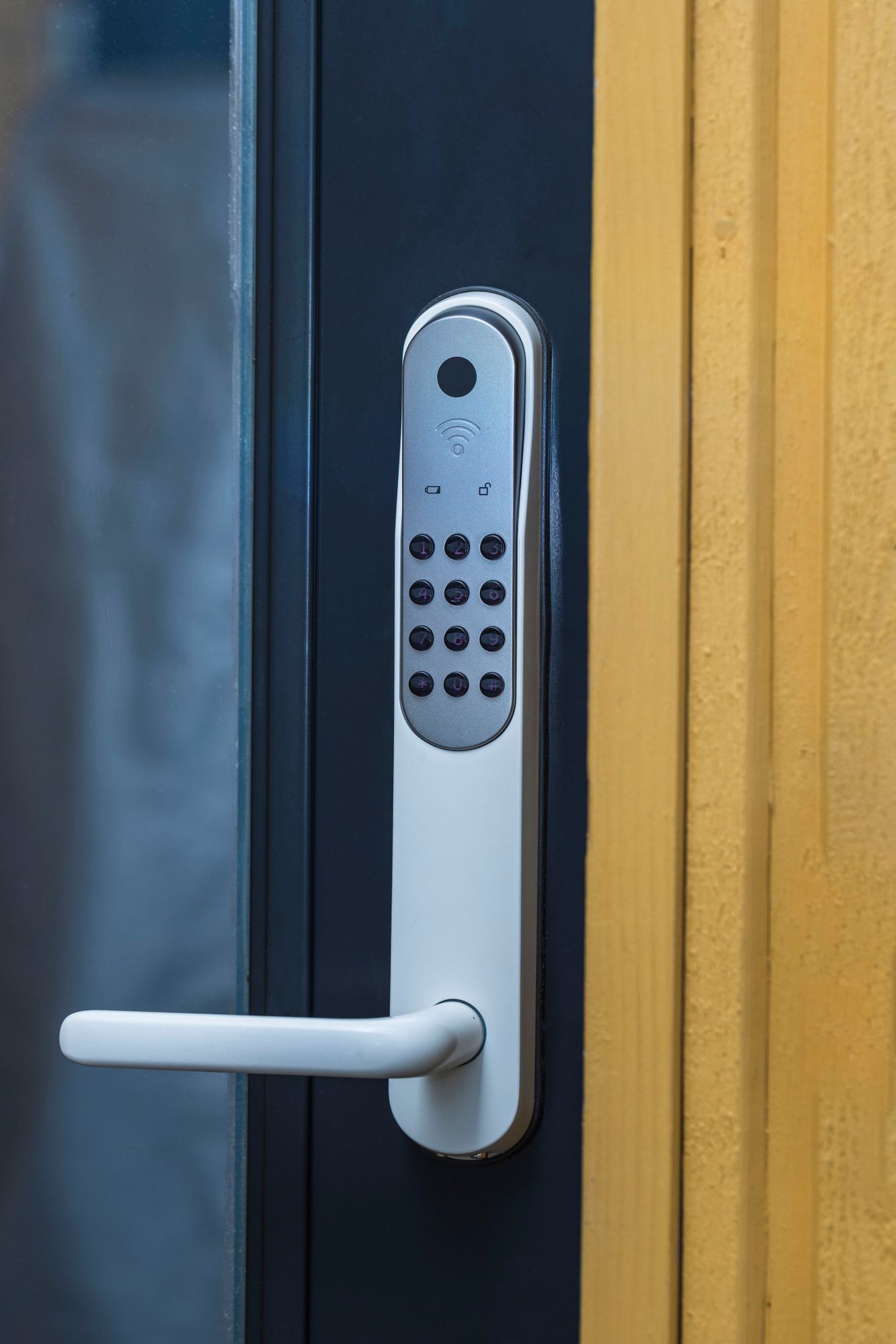 Cerradura de puerta con teclado blanco y manija sobre un marco de puerta negro, montada en una puerta amarilla.