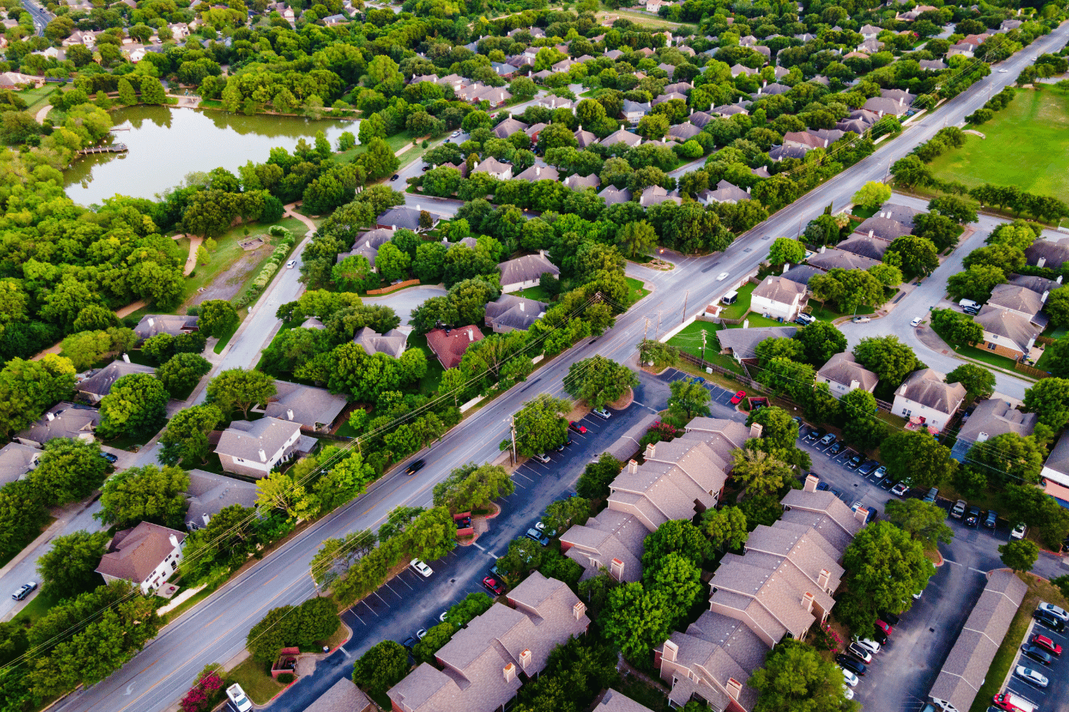 Aerial view of a suburban neighborhood with houses, a road, trees, and a lake.