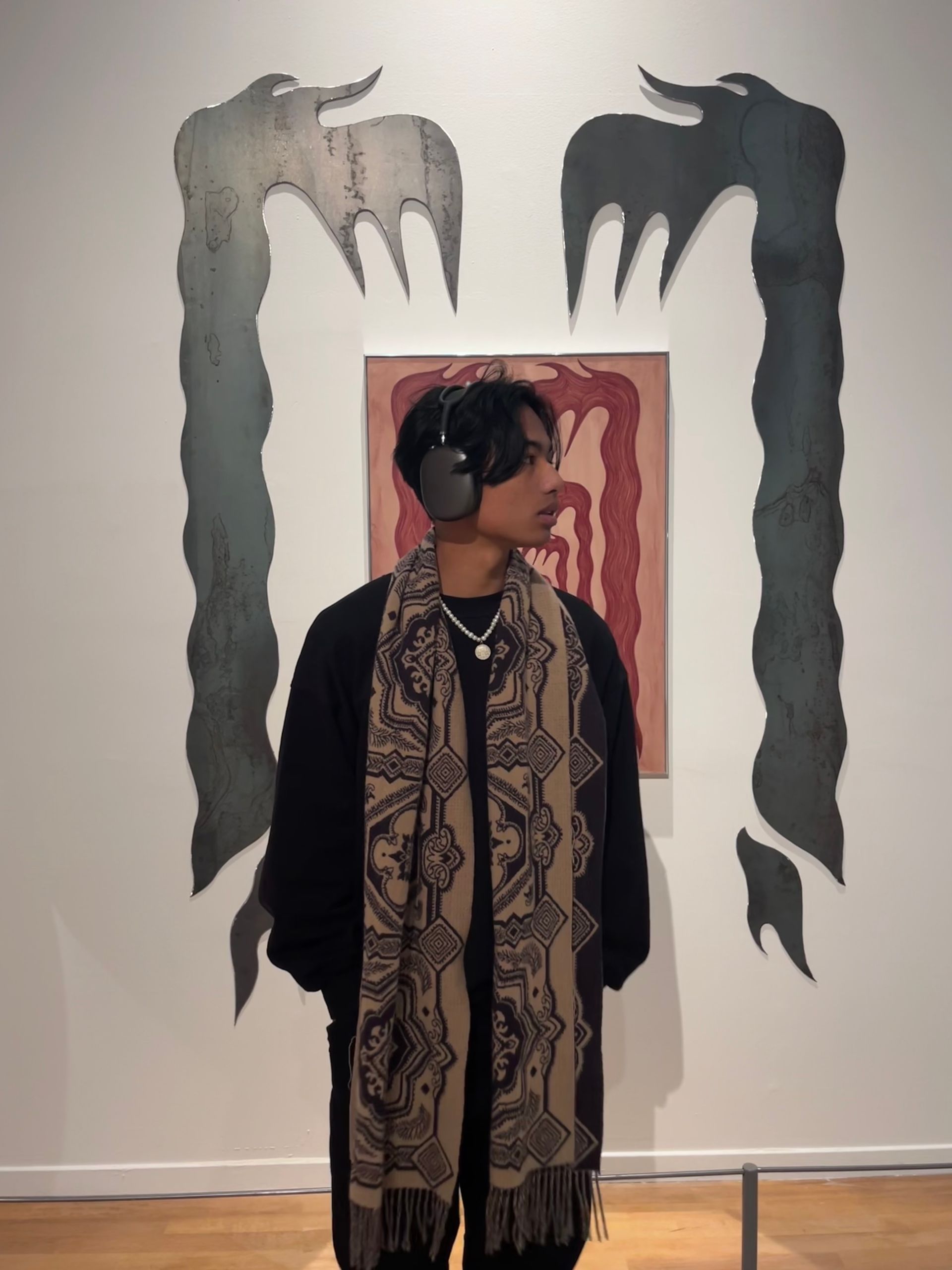 Un homme vêtu de noir et portant une écharpe se tient devant une œuvre d'art abstrait dans une galerie.