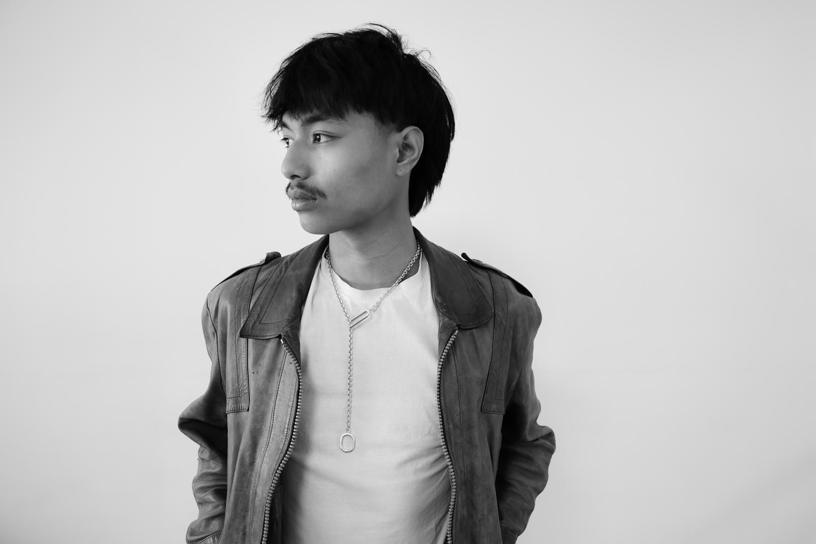 Un homme à la fine moustache, portant une veste sur une chemise blanche, regarde sur le côté.