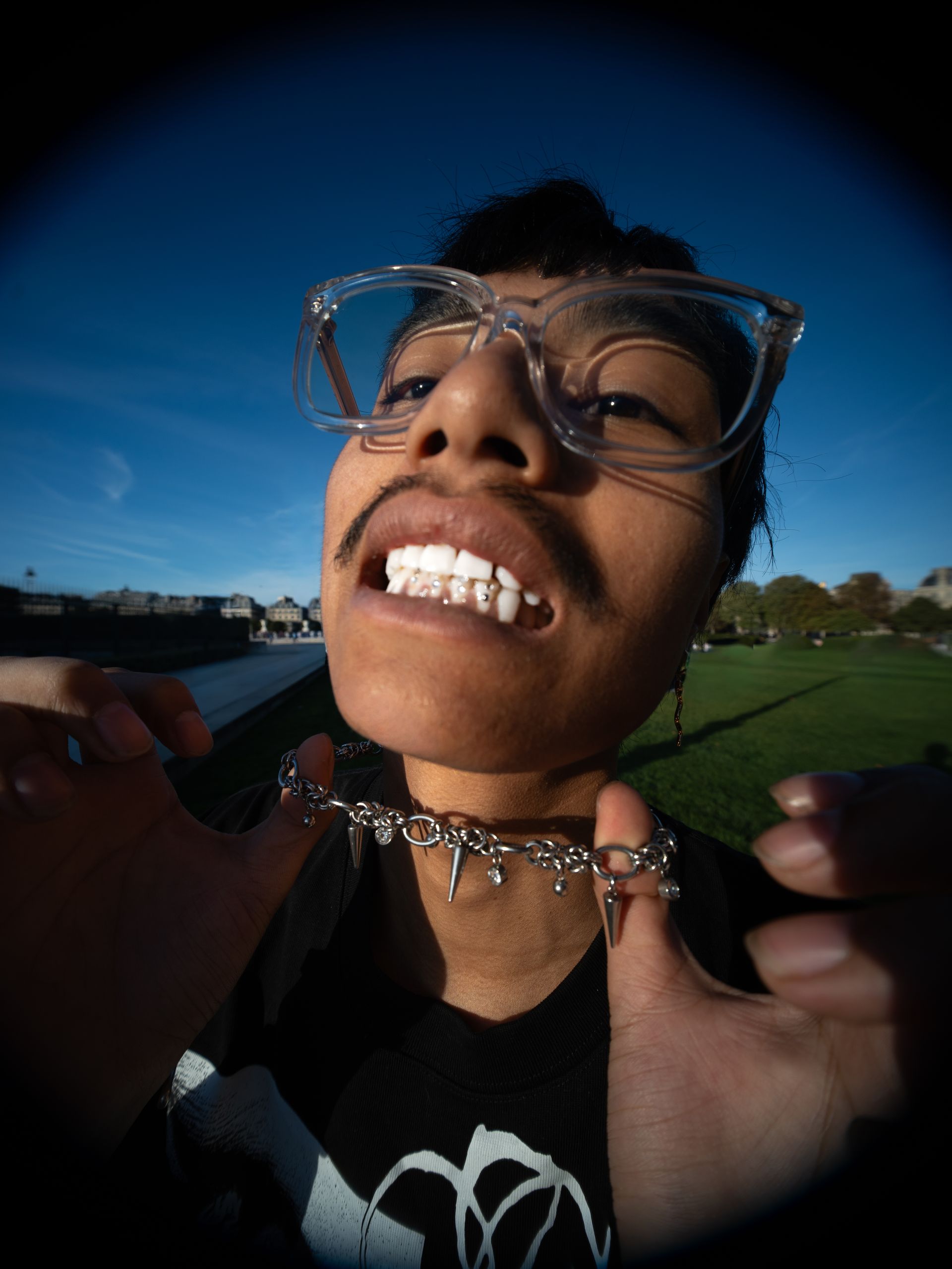 Une personne saute dans les airs, exécutant un mouvement de danse dans une rue. Bâtiments, arbres et ciel bleu.