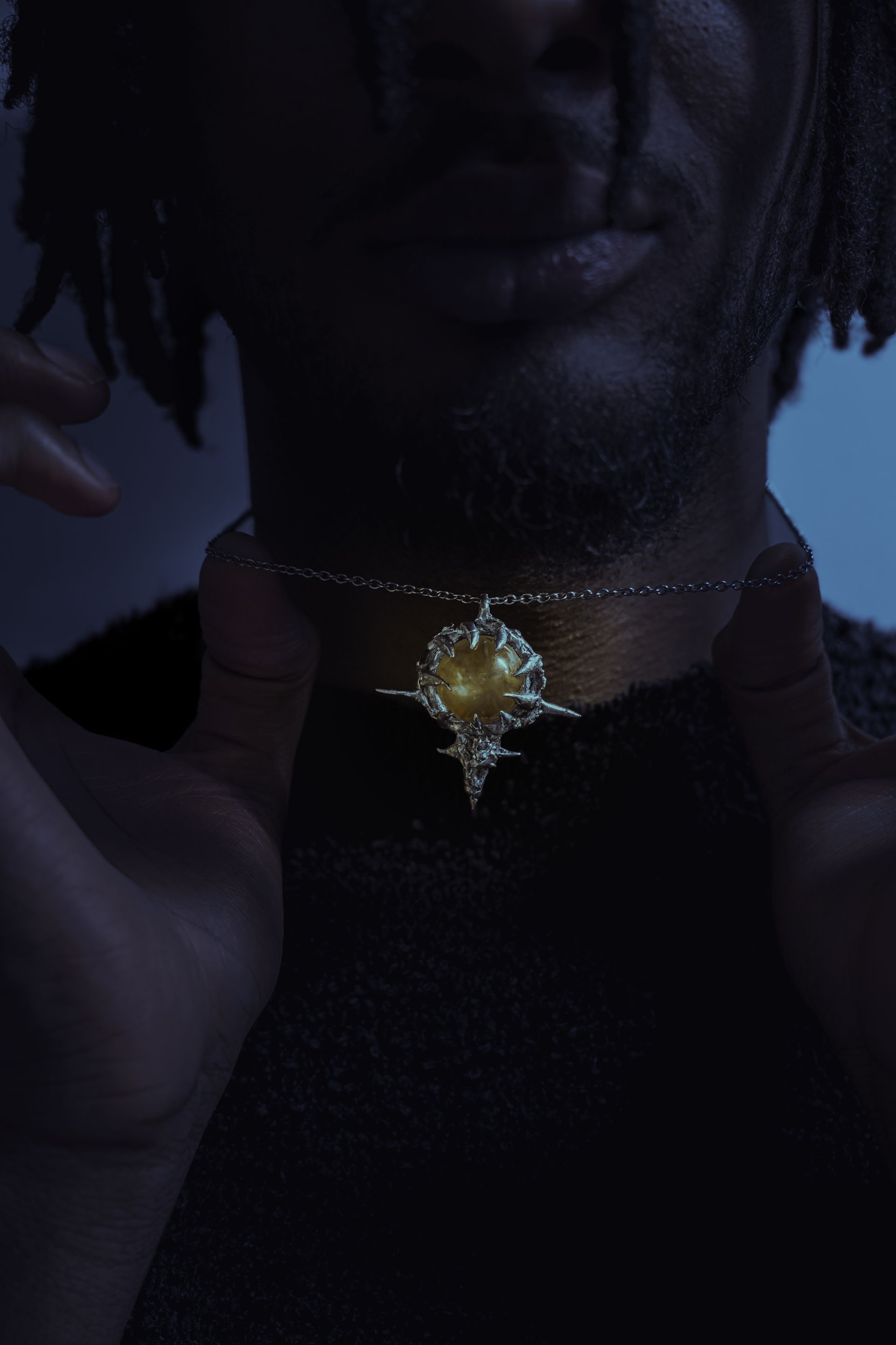 Personne portant un collier en argent avec un pendentif central à pointes, les mains encadrant le collier.