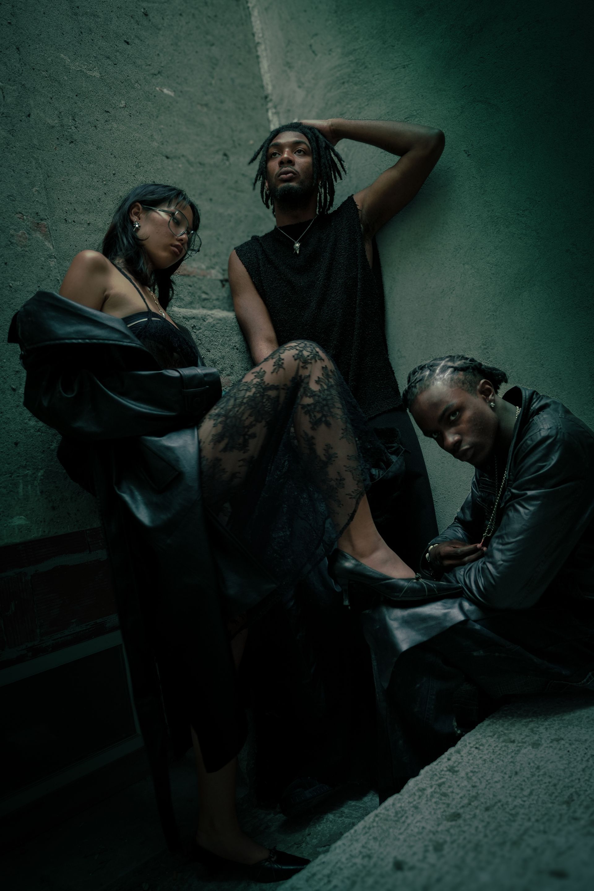 Trois personnes vêtues de sombre posent sur des marches en béton, appuyées l'une contre l'autre et le regard perdu.