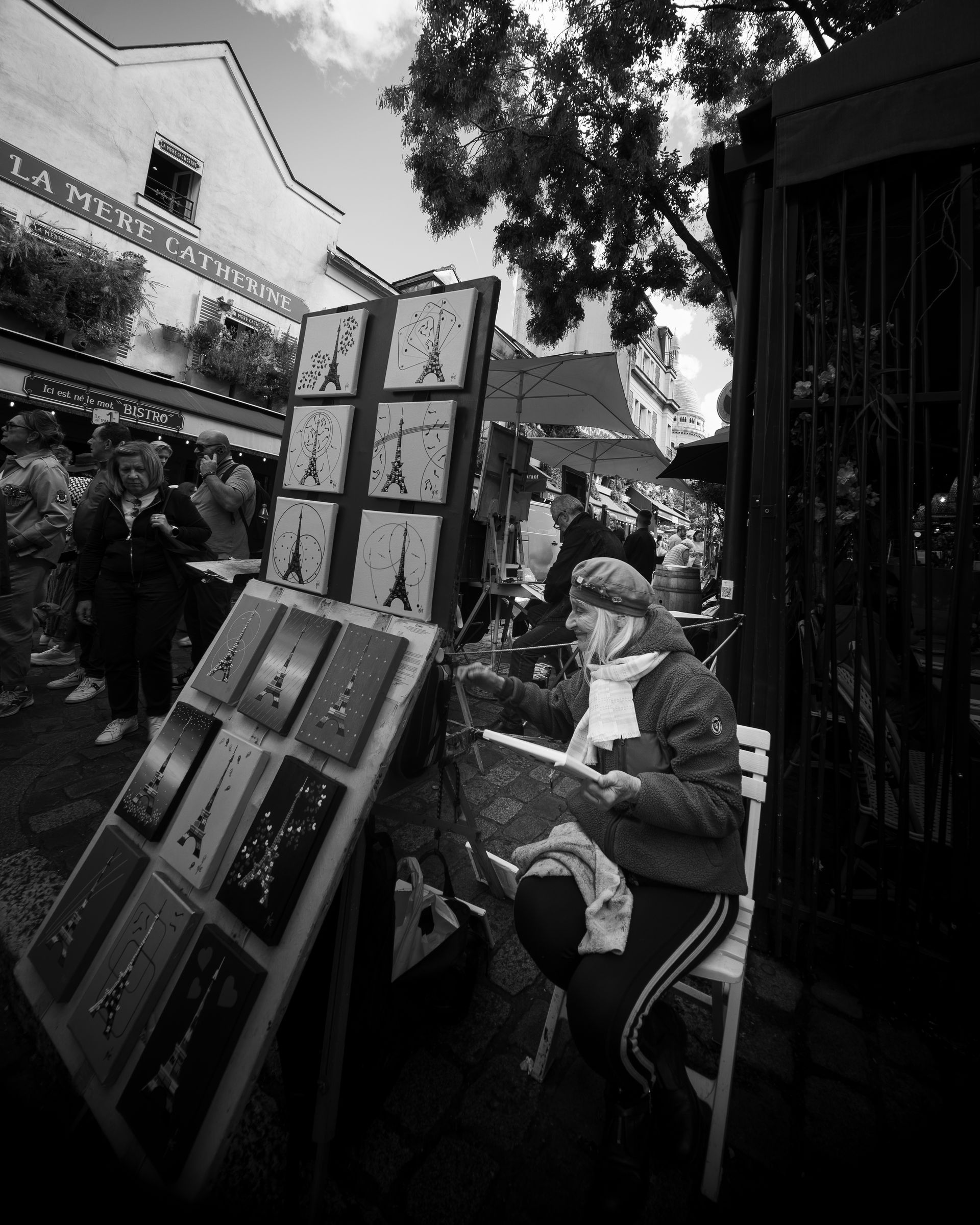 Un artiste de rue peint près d'une exposition d'art représentant la Tour Eiffel ; décor parisien.