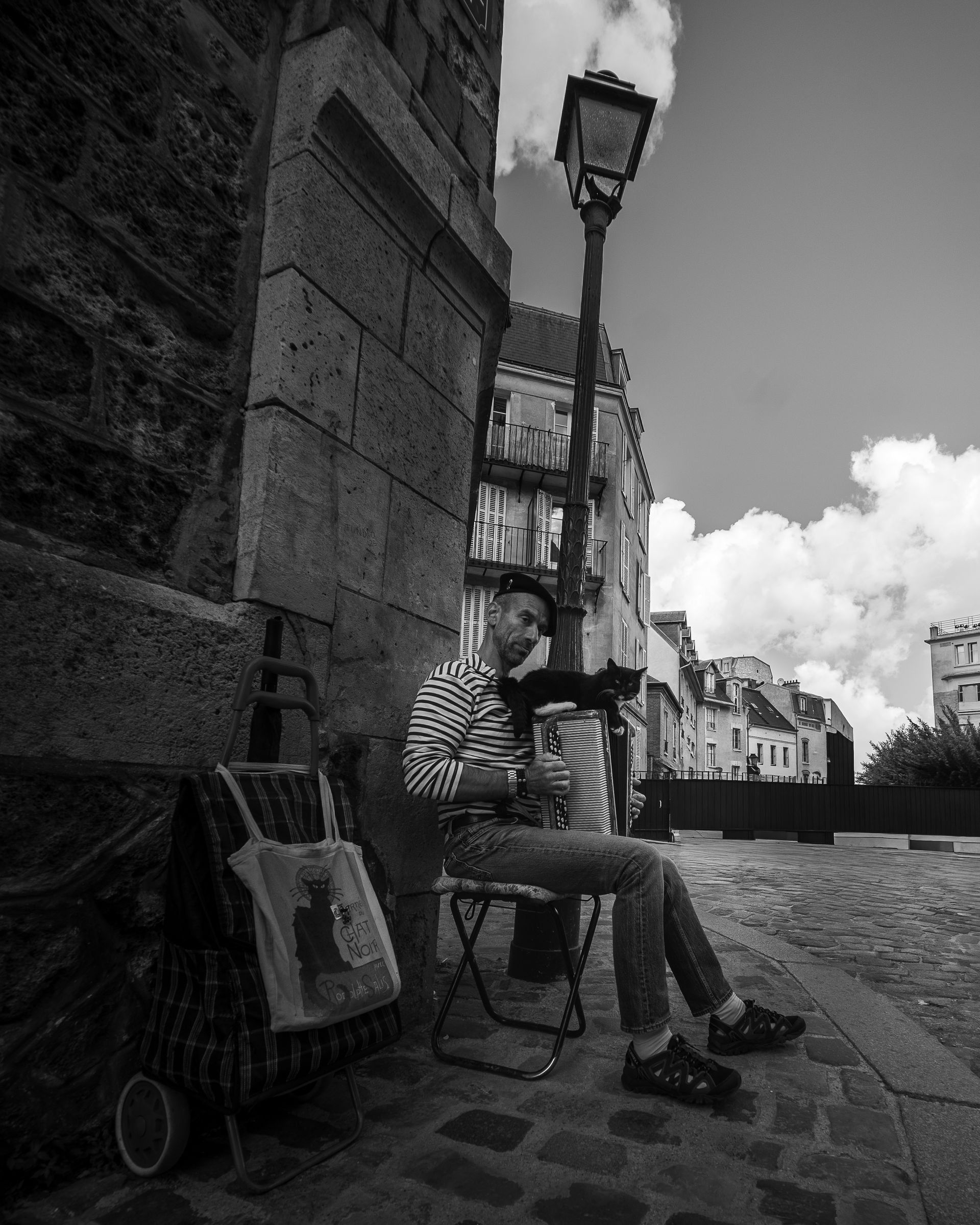 Un homme est assis dehors, une tasse à la main, près d'un chariot et d'un lampadaire.