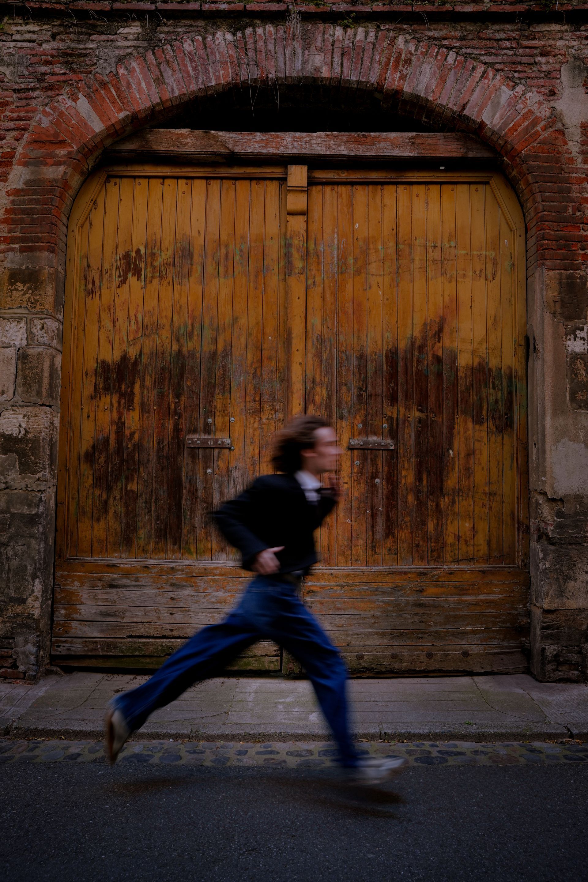 Un homme court devant une porte jaune défraîchie et une entrée en briques voûtée.