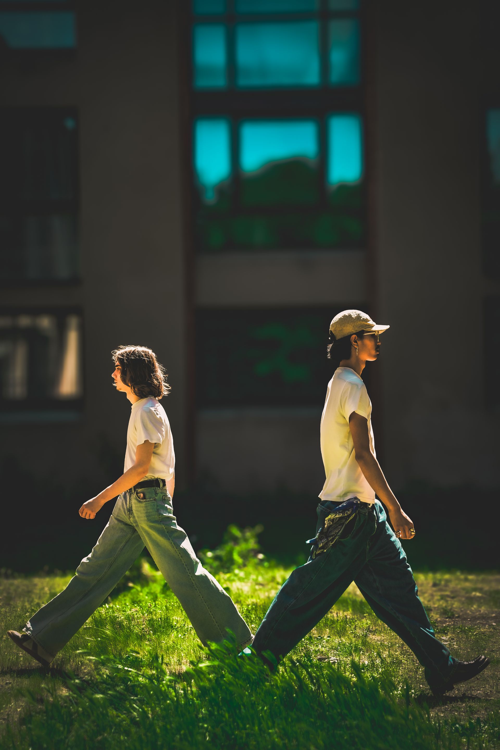 Deux personnes marchent sur la pelouse devant un bâtiment. L'une d'elles porte un chapeau.