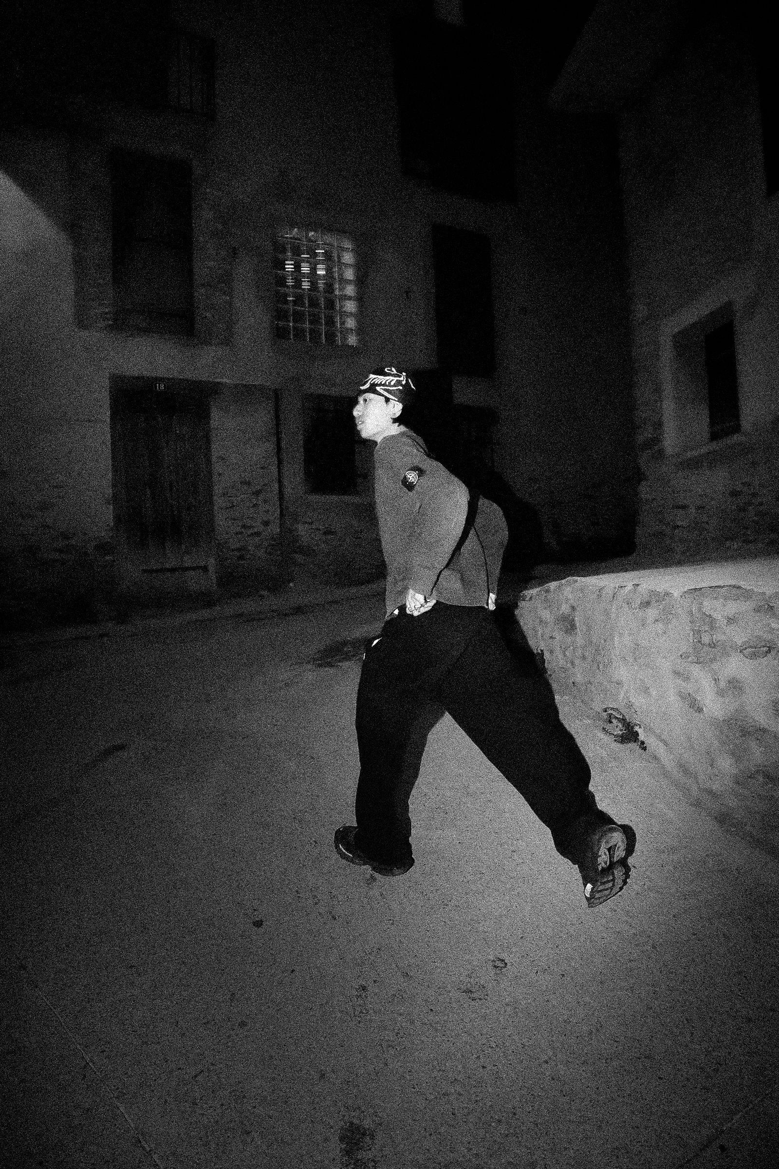 Une personne marchant dans une ruelle sombre la nuit, portant une casquette et des vêtements sombres. 